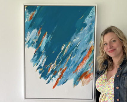 Woman with blonde hair smiling next to an abstract painting with blue, white, and orange brushstrokes.