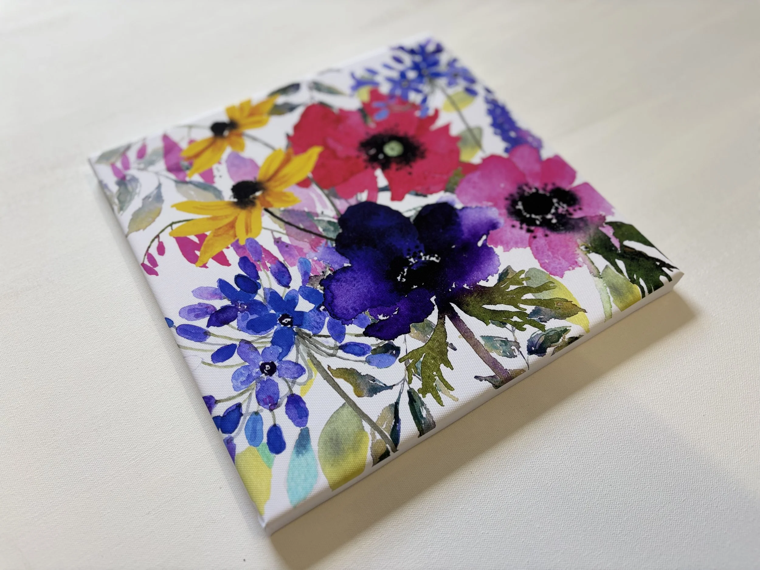 A rectangular item with a vibrant watercolor floral pattern, featuring pink, purple, yellow, and blue flowers on a white background, lying on a plain white surface.