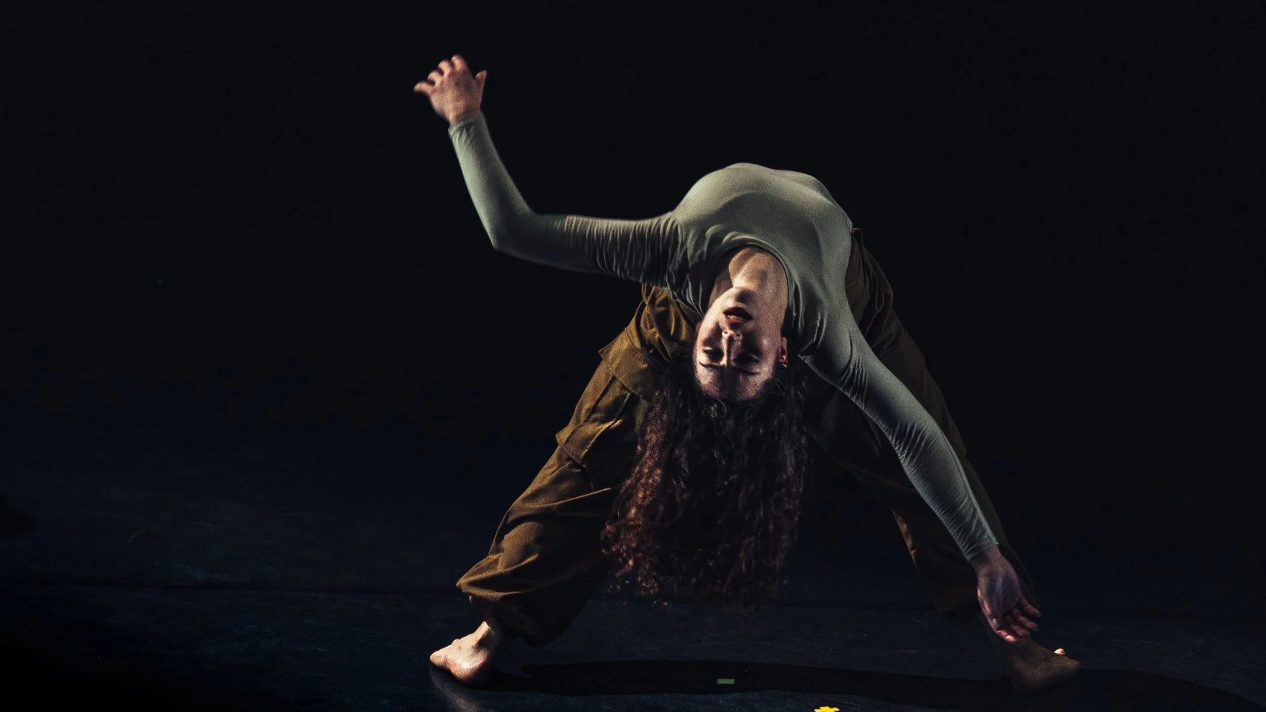 Une personne danse ou performe une pose artistique dans un espace sombre.