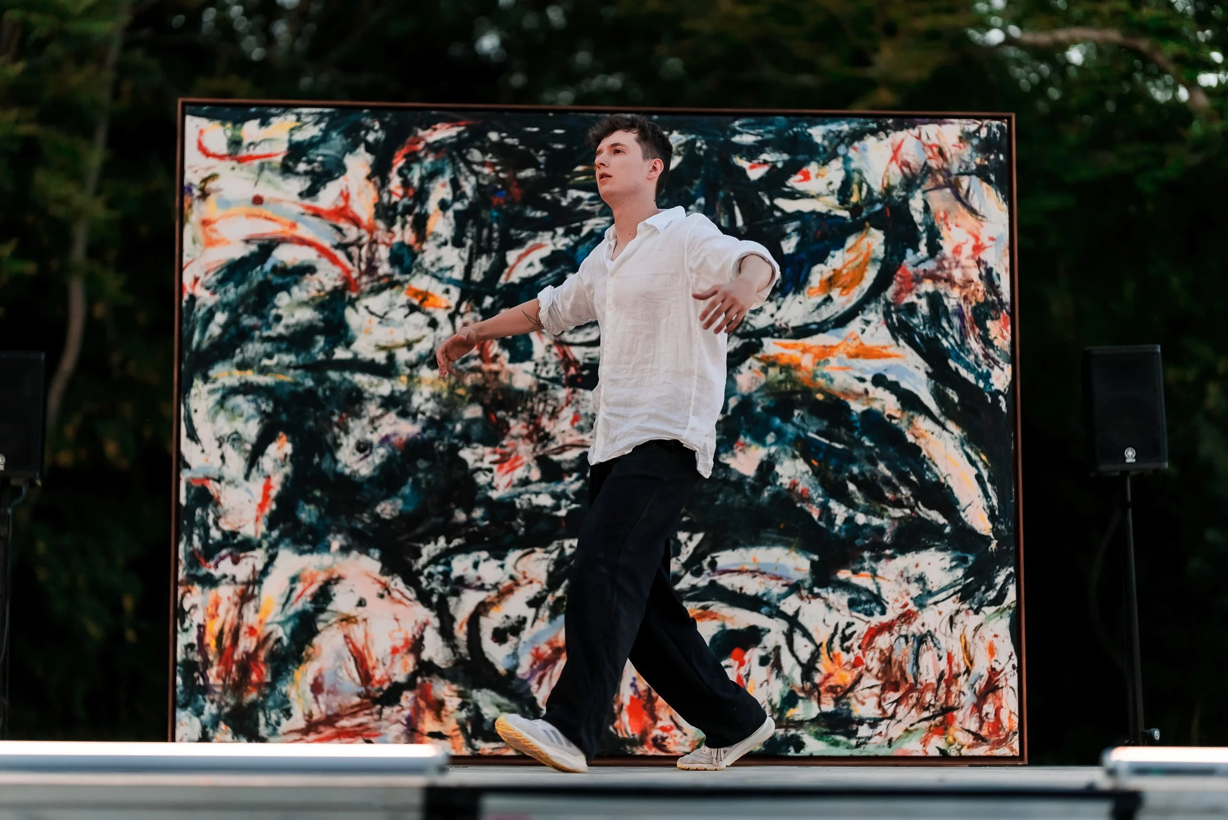 Un jeune homme danse devant une toile d'art abstrait dans un environnement extérieur.