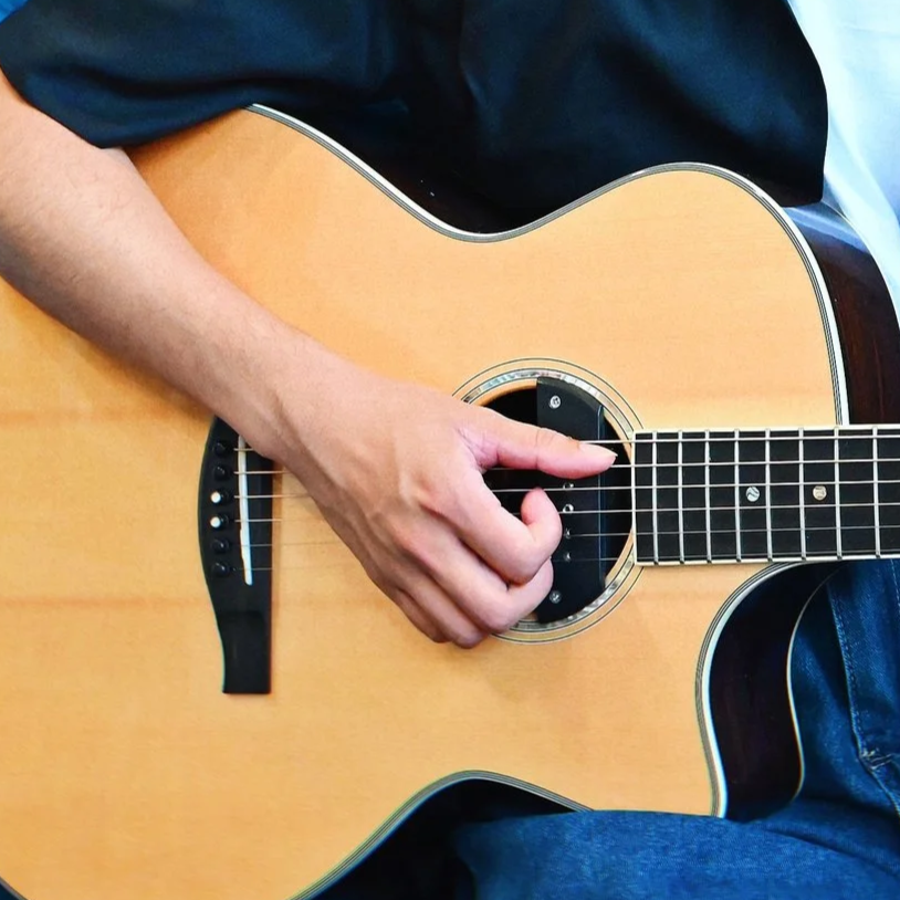 Close-up of a person playing an acoustic guitar, focusing on their left hand on the fretboard.