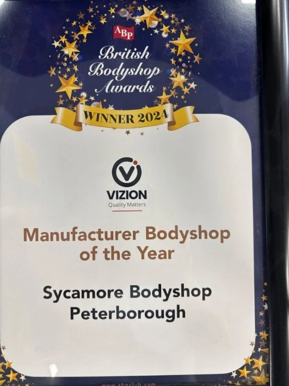 Award poster for the British Bodyshop Awards 2024, recognizing Sycamore Bodyshop in Peterborough as Manufacturer Bodyshop of the Year, with a dark blue background and gold stars.