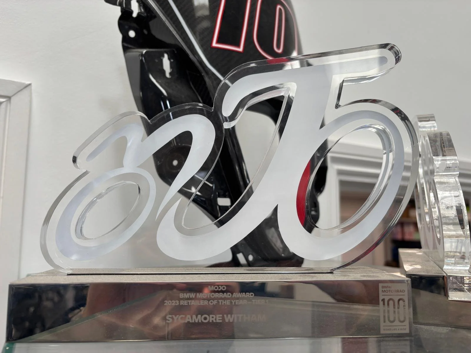 A crystal award displaying the number 125 with the word 'WOW' at the top, placed on a reflective surface with a black motorcycle helmet in the background.