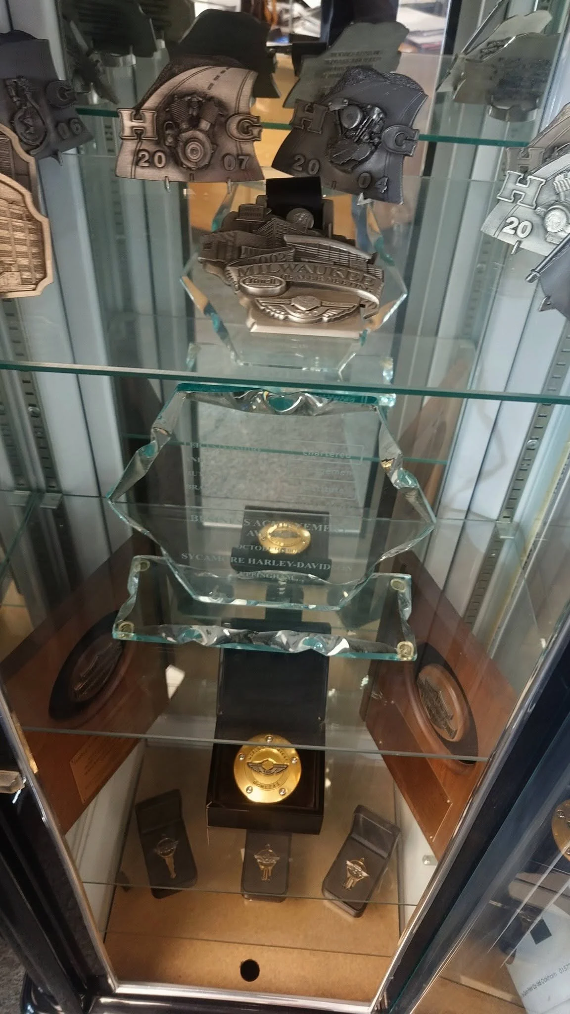 Display case with Harley-Davidson memorabilia including trophies, plaques, and decorative items.
