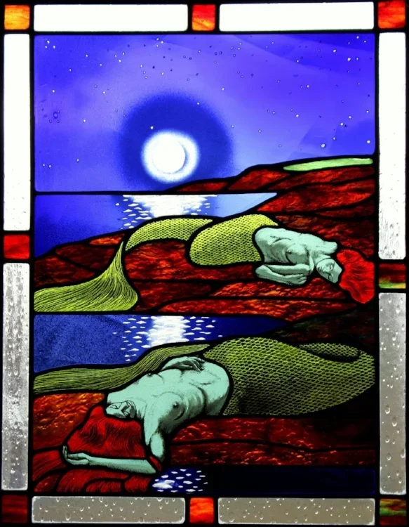 glass panel of mermaids laying on red rocks