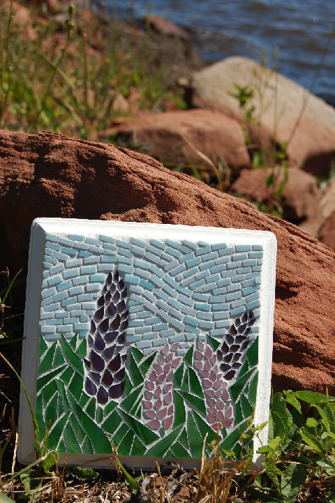 glass mosaic lupin panel resting on the rocks at the shore
