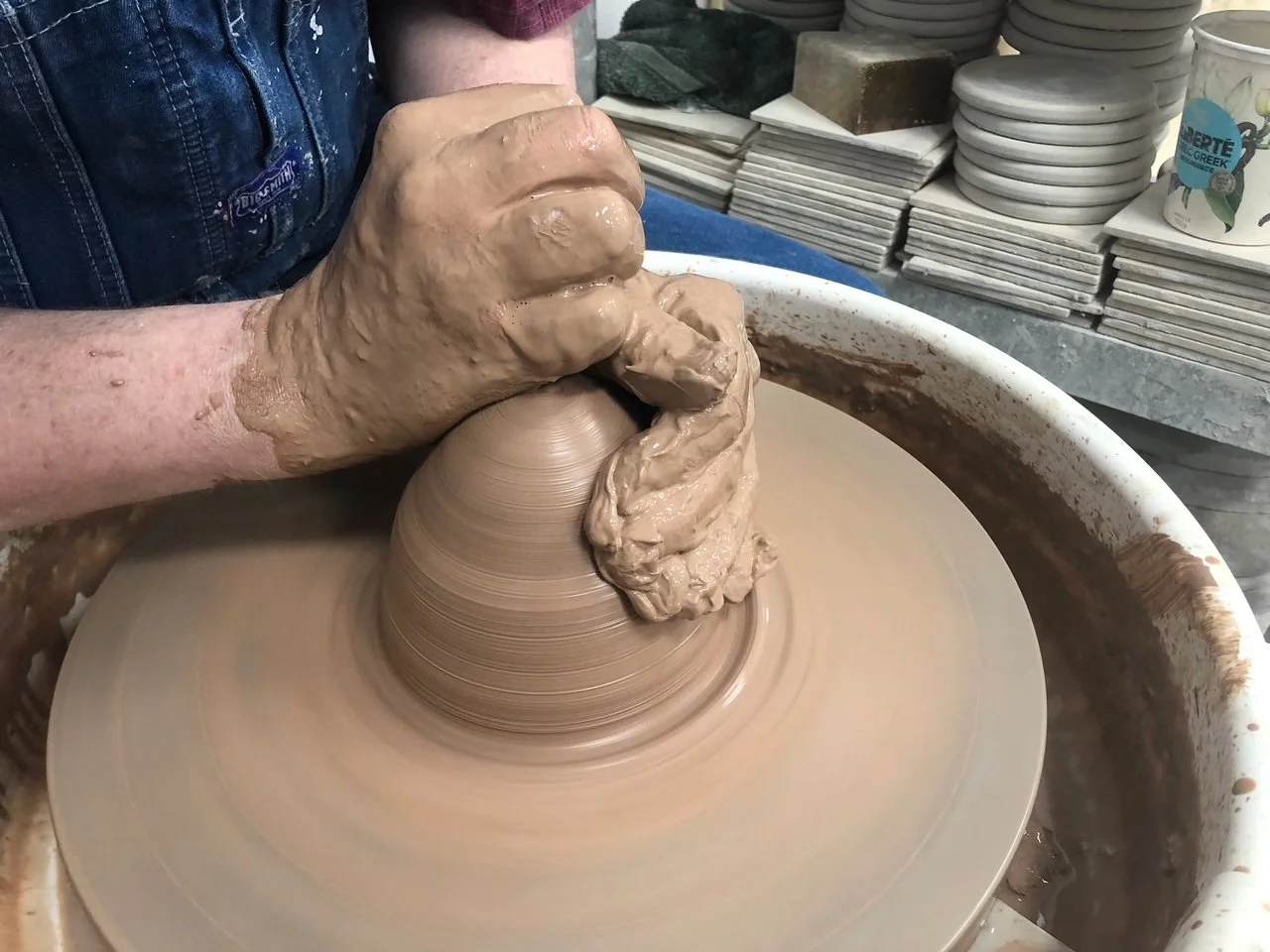 clay covered hands and a pottery wheel
