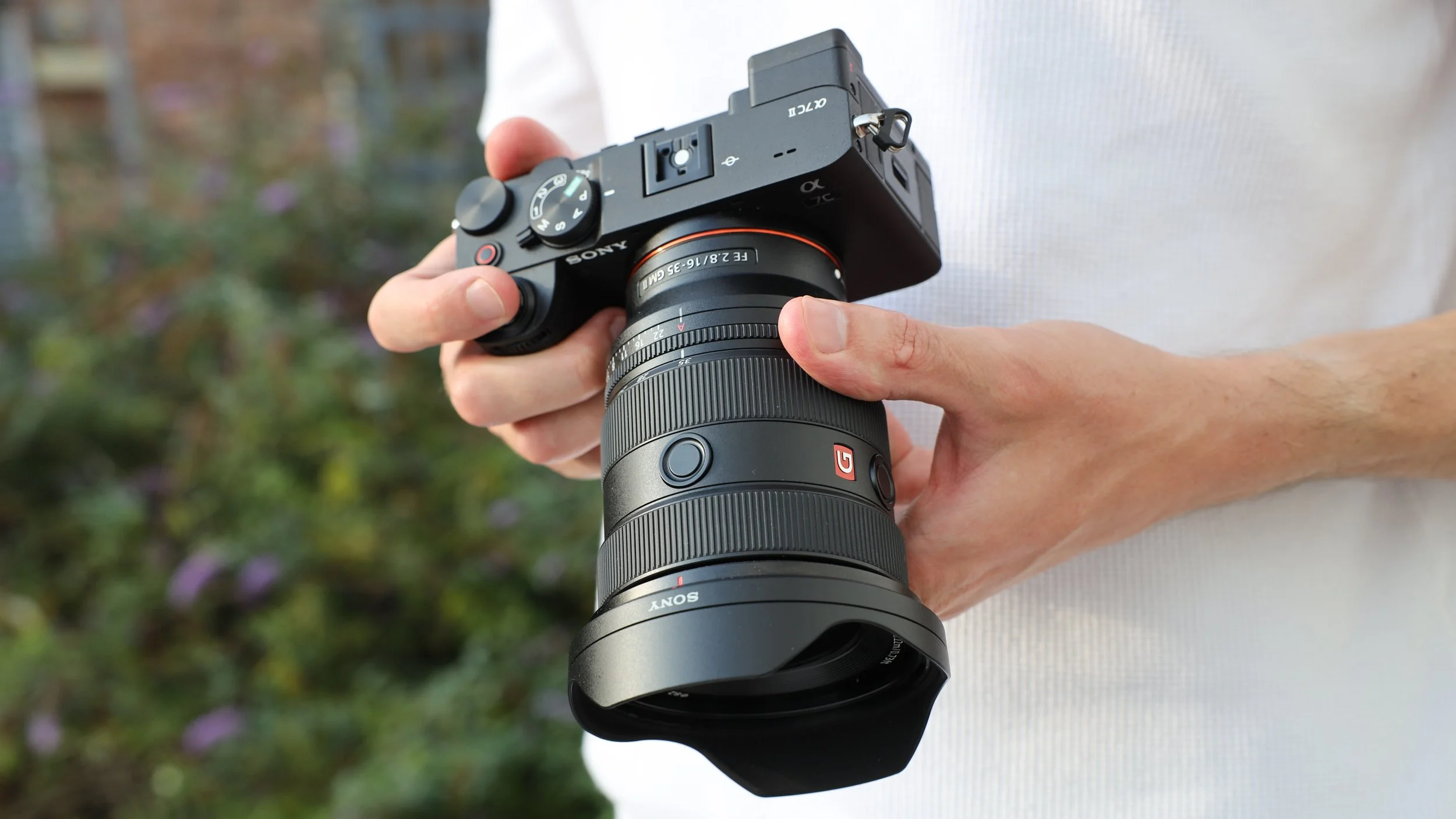 Person holding a Sony mirrorless camera with a large telephoto lens outdoors.