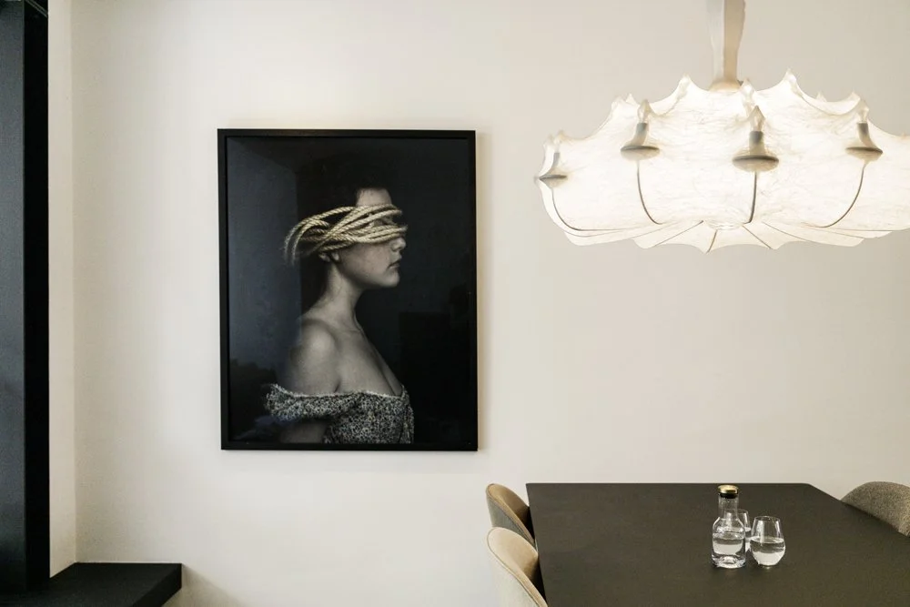 Dining area with portrait artwork and sculptural pendant lighting in a De Pijp apartment in Amsterdam