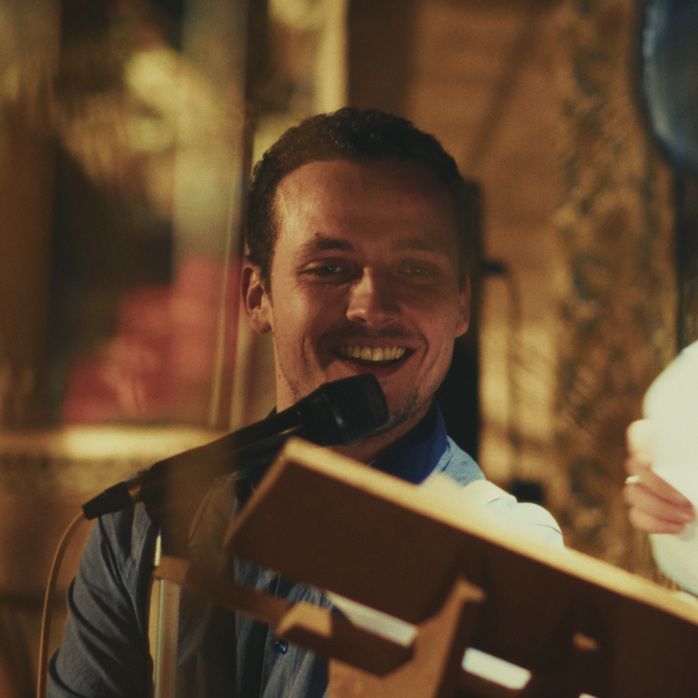 Un homme souriant tenant un livre, avec un microphone devant lui, dans une ambiance chaleureuse.
