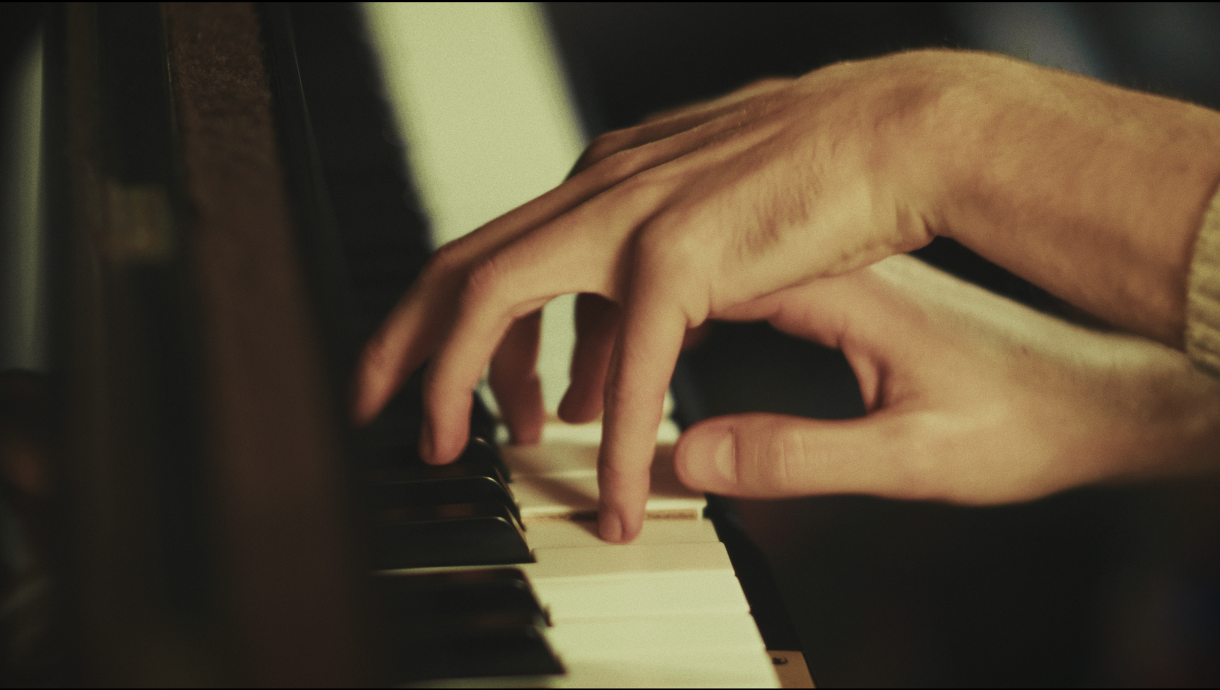 Deux mains jouent du piano, l'une plus grande et l'autre plus petite, suggérant peut-être un adulte et un enfant.