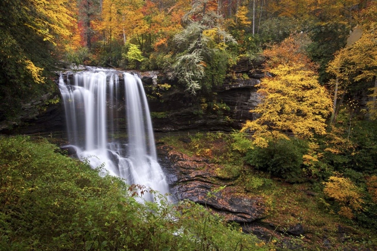 A waterfall flowing over rocks surrounded by trees with colorful autumn leaves.