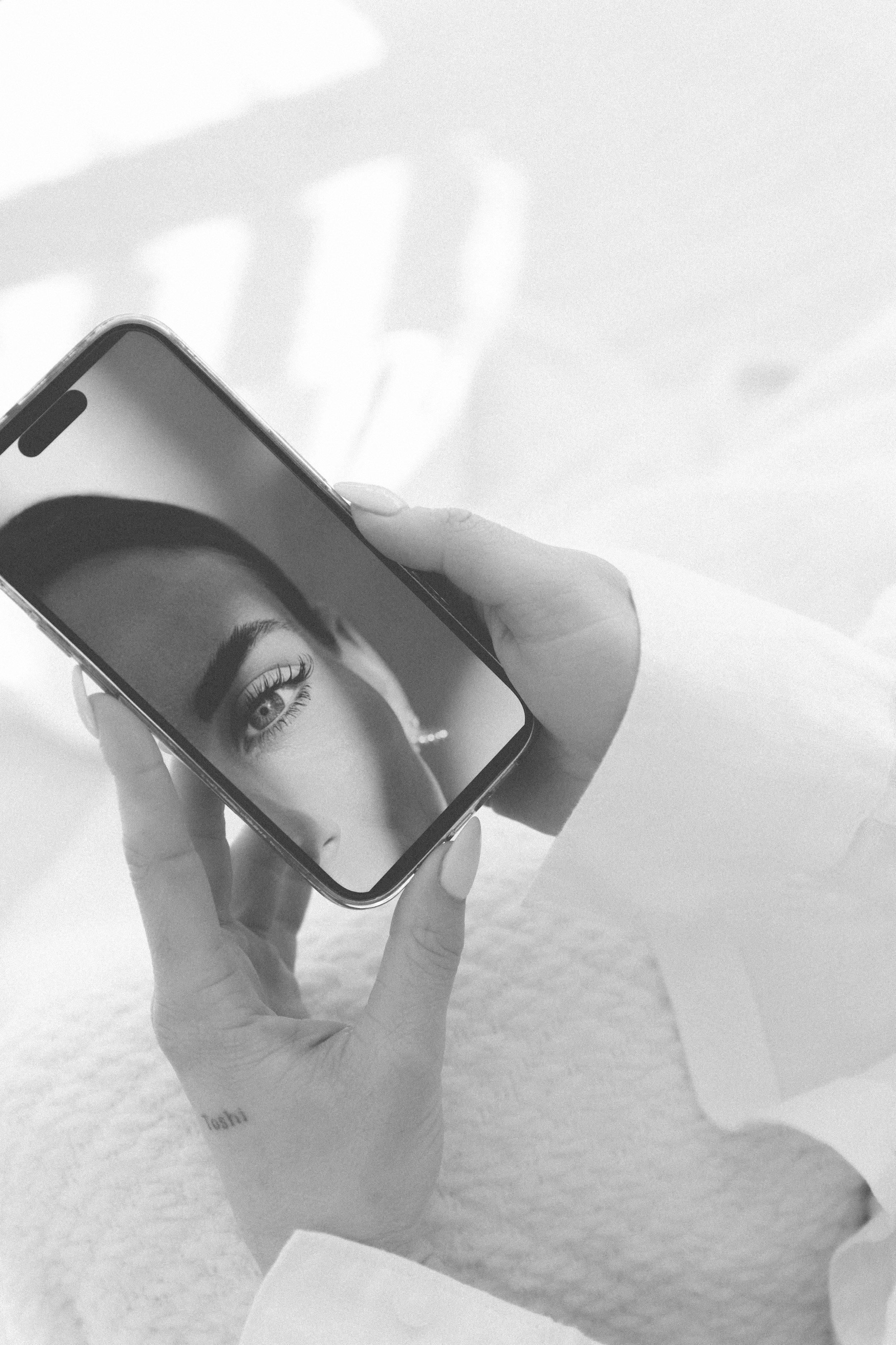A person holding a smartphone displaying a close-up photo of a woman's eye with styled eyelashes.