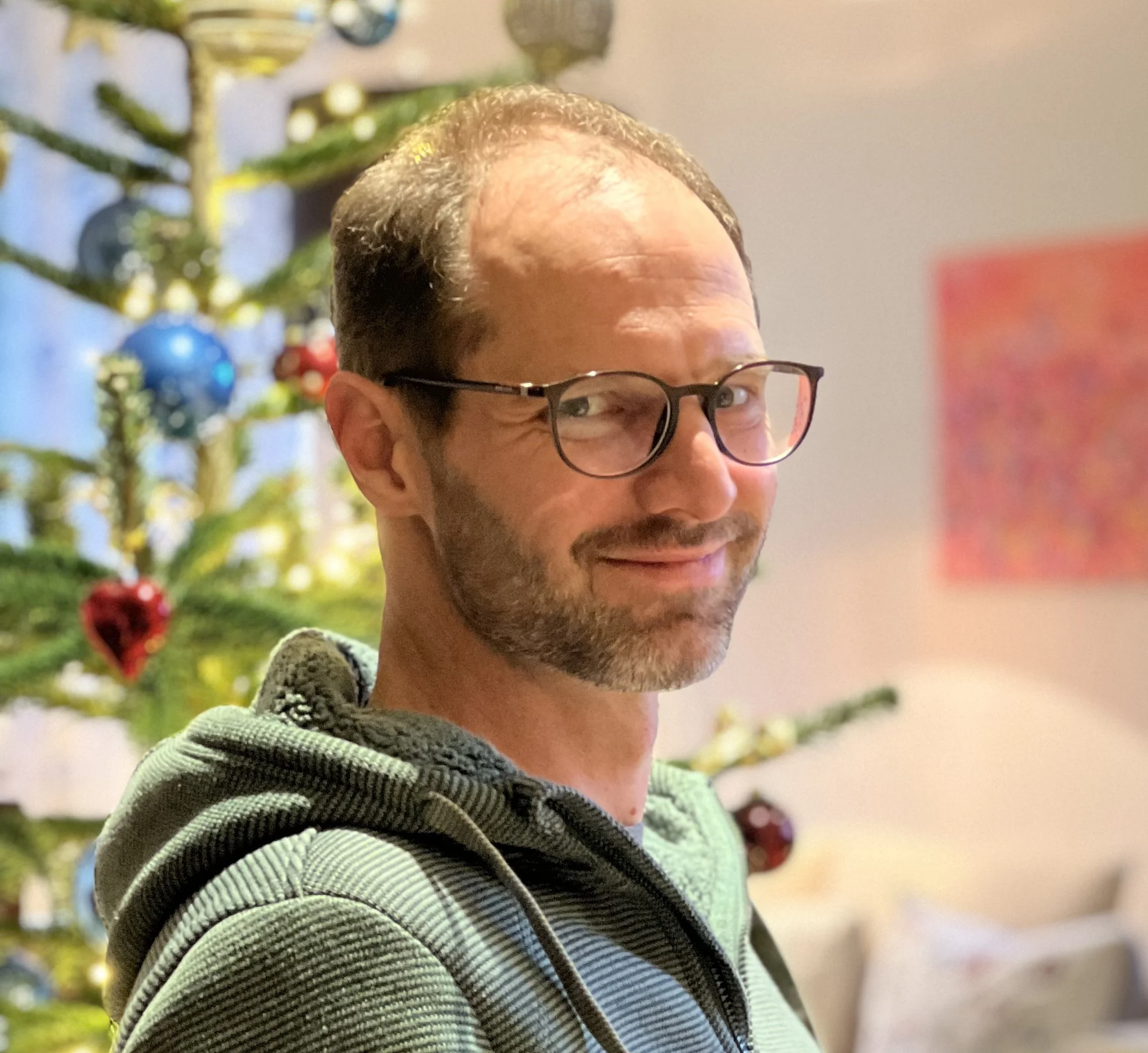Nahaufnahme eines Mannes mit Brille, der eine schwarze und graue gestrickte Jacke trägt.