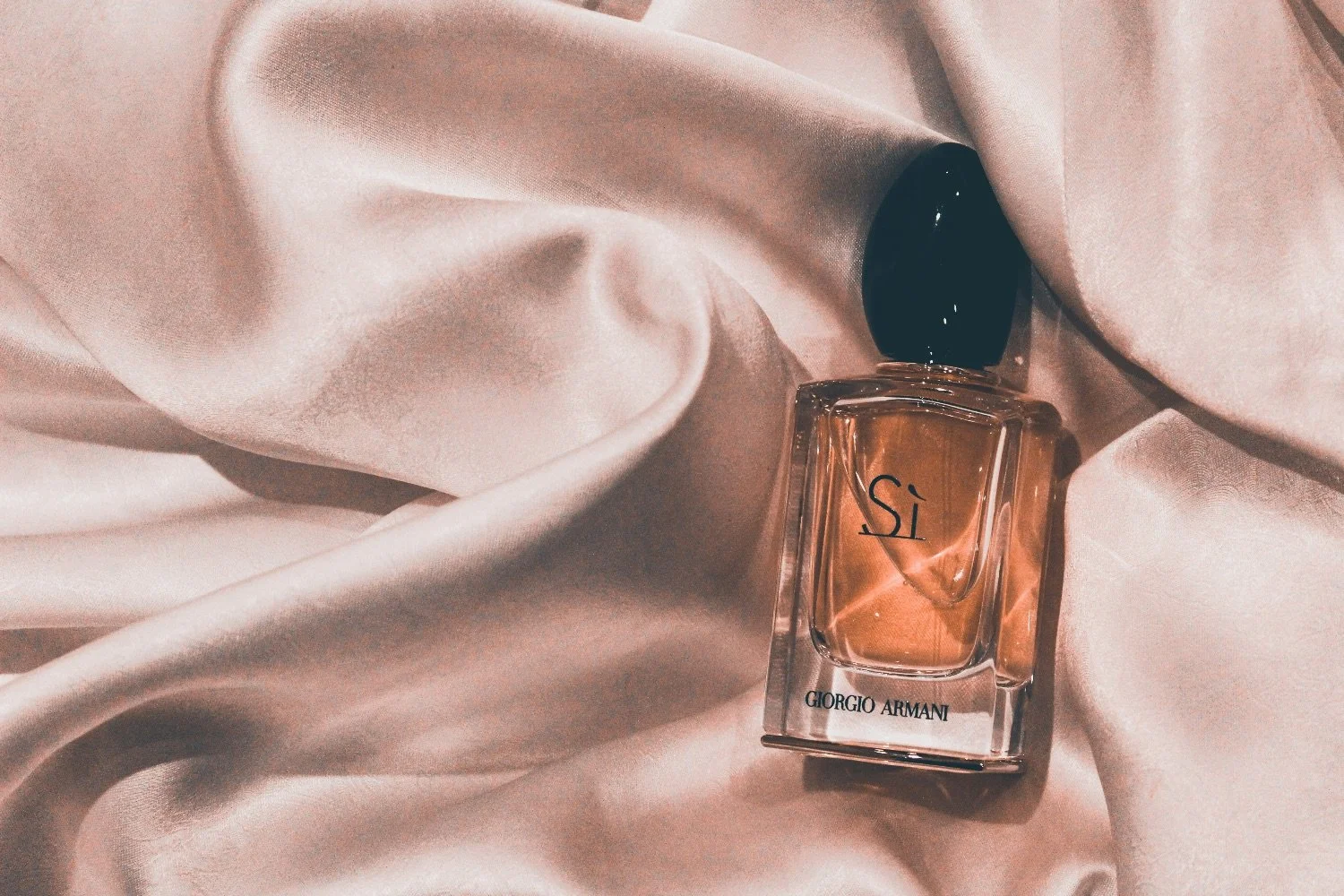 A bottle of Giorgio Armani Si perfume lying on soft pink satin fabric.