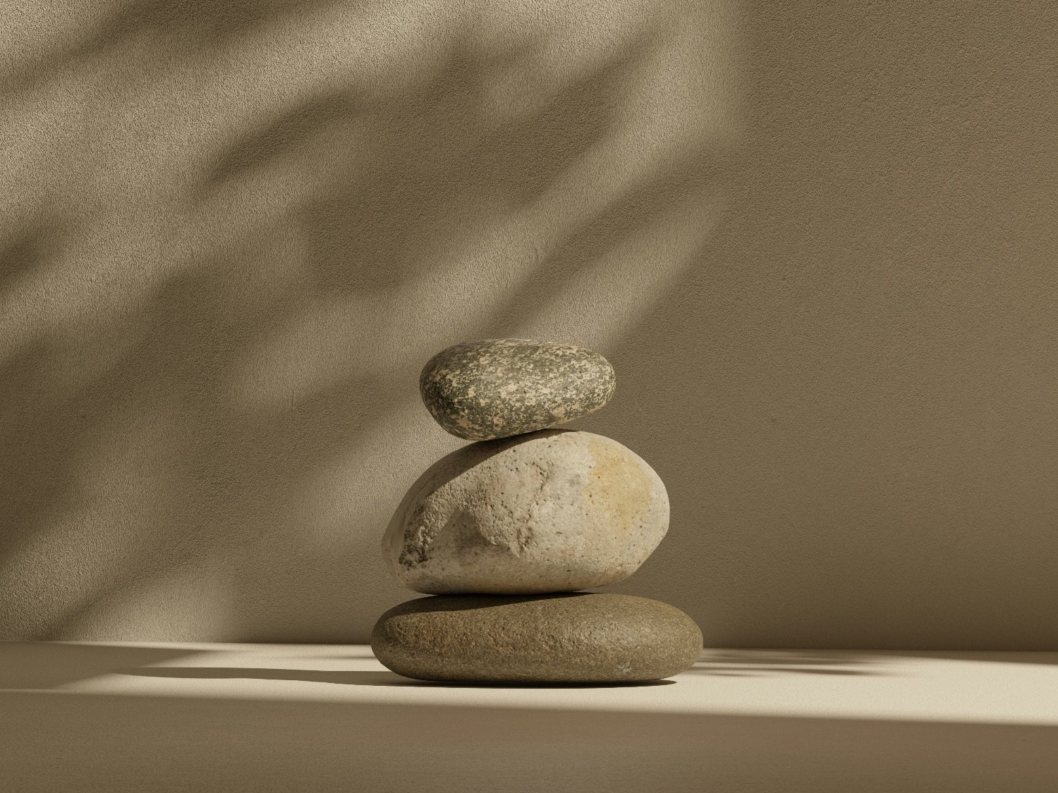 Three smooth stones stacked on top of each other against a beige background, with soft shadows cast on the wall.