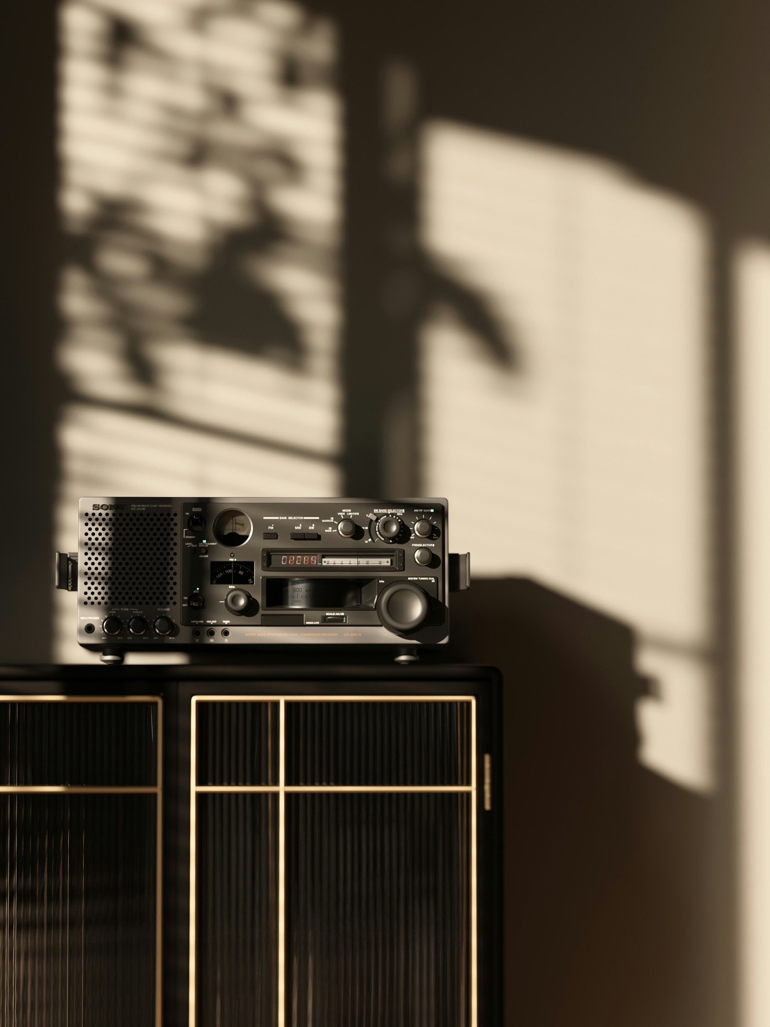 A vintage radio on top of a black cabinet with gold accents, casting shadows of window blinds on the wall behind.