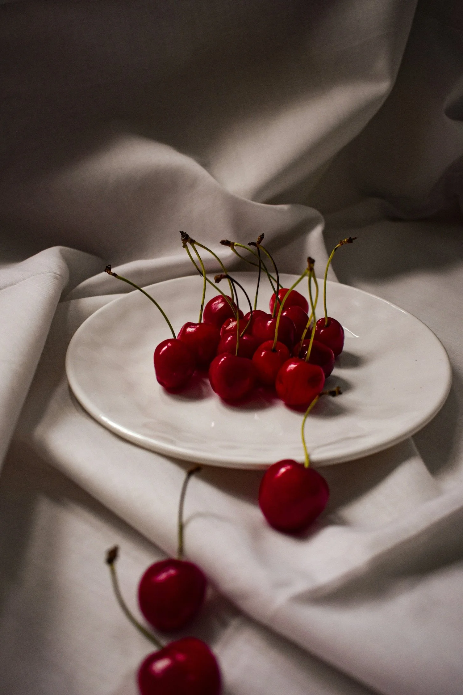 A white plate with red cherries on a white cloth background.