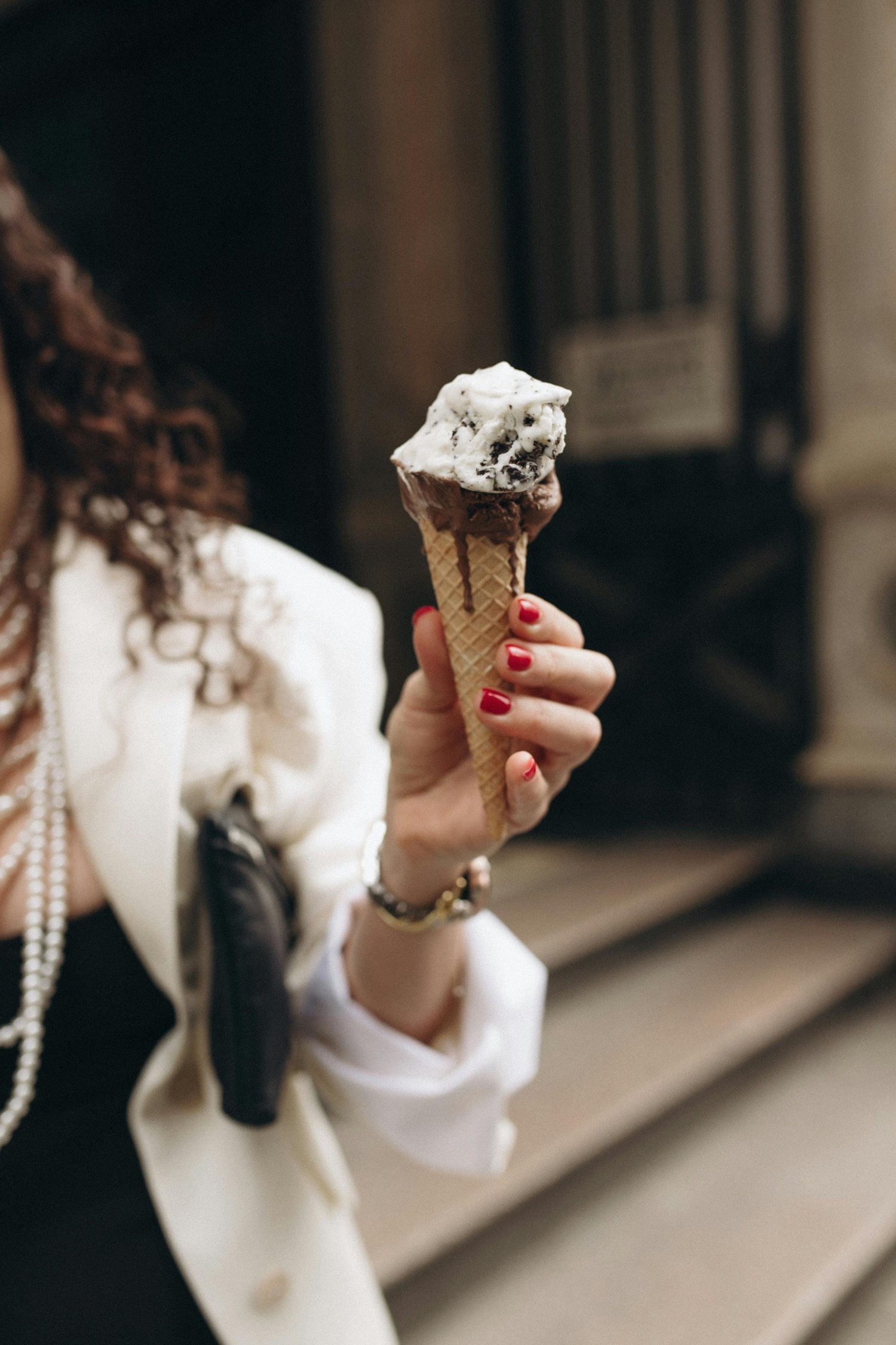 A person holding an ice cream cone with vanilla and chocolate ice cream, inside a building with marble steps.