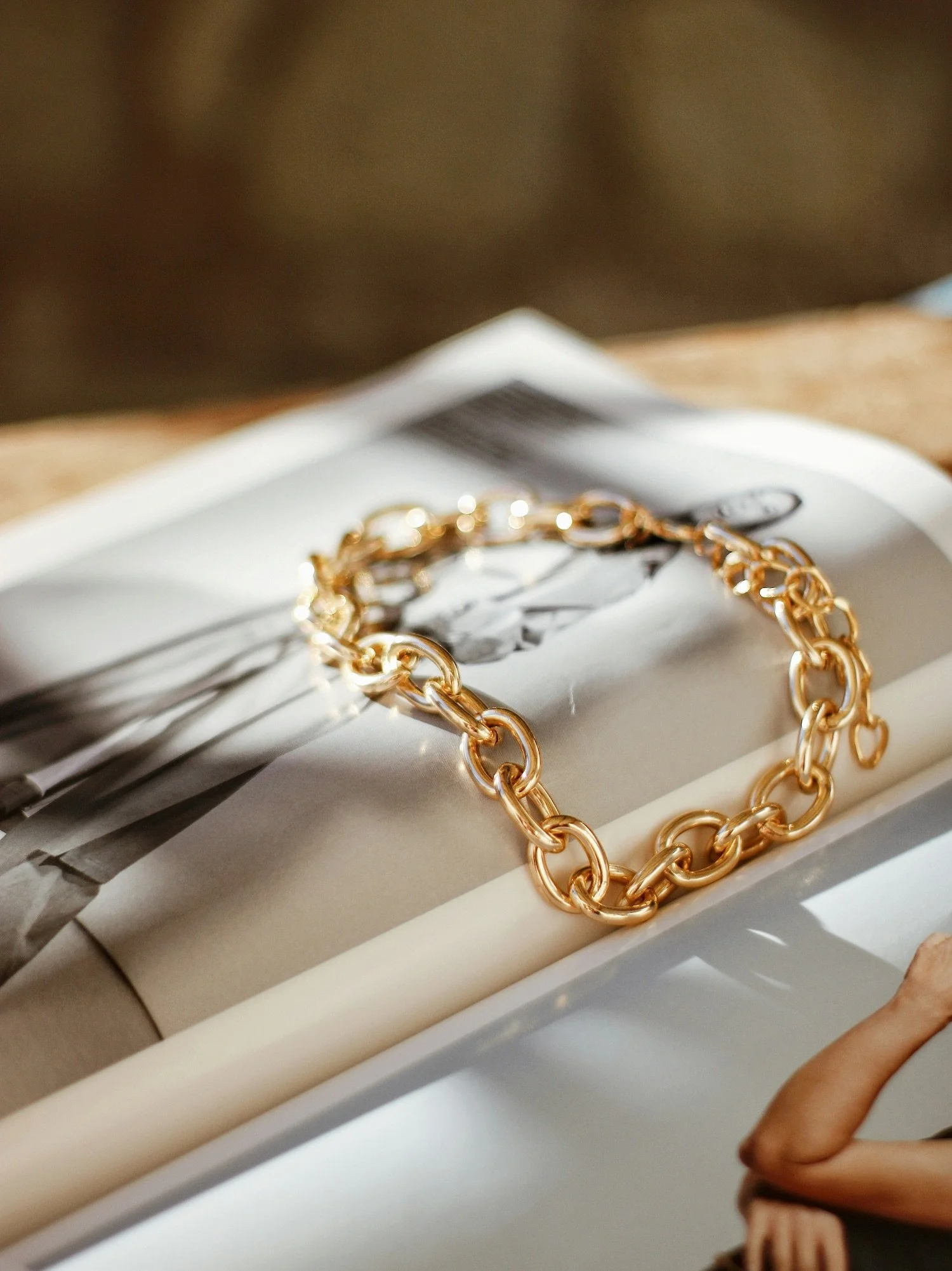 A gold chain bracelet resting on an open magazine with black and white photos, on a white surface.