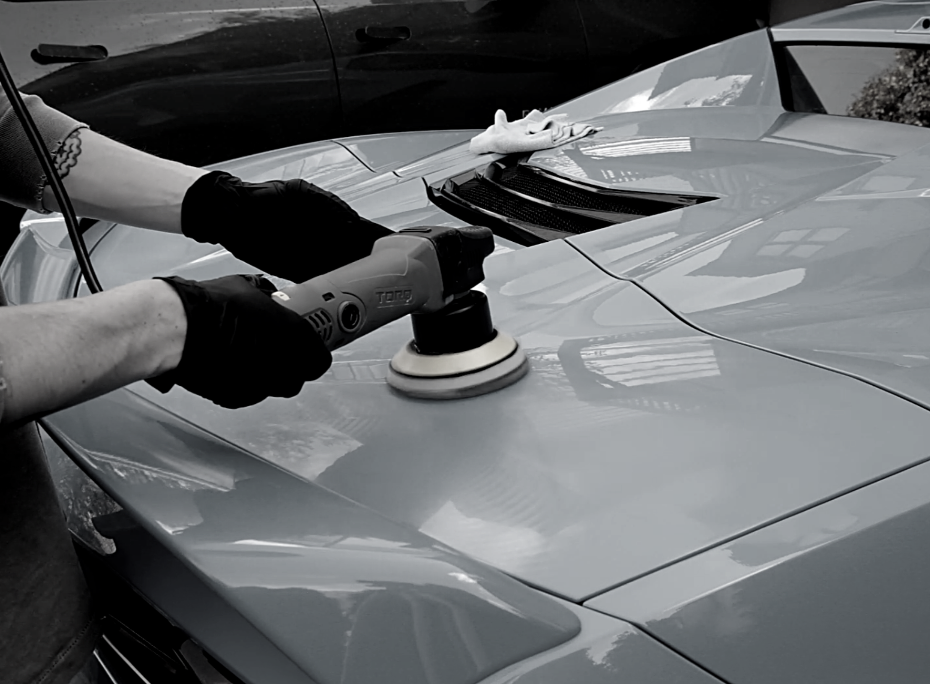 Person polishing a sleek sports car with a buffer tool, wearing a black glove and a bracelet.
