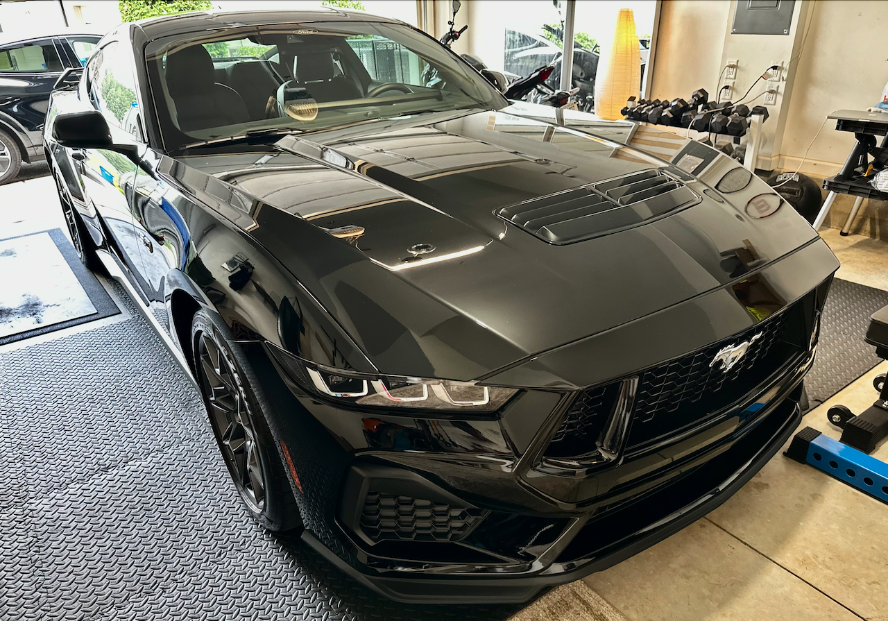 A black Ford Mustang sports car parked inside a garage or showroom with a fitness equipment area in the background.