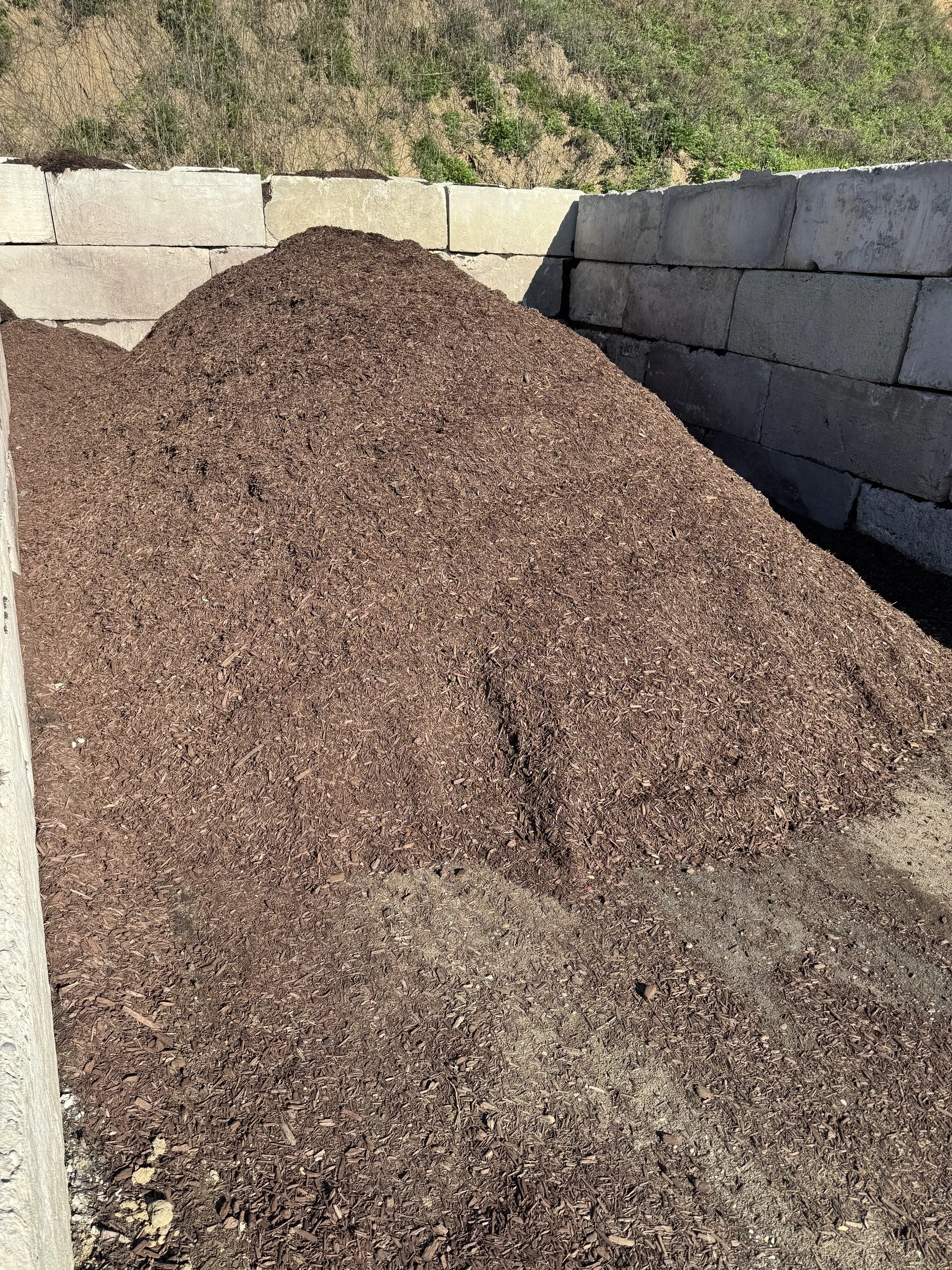 A pile of mulch in a enclosed outdoor area at Sandlot stone block wall and a background of green trees at Sandlot