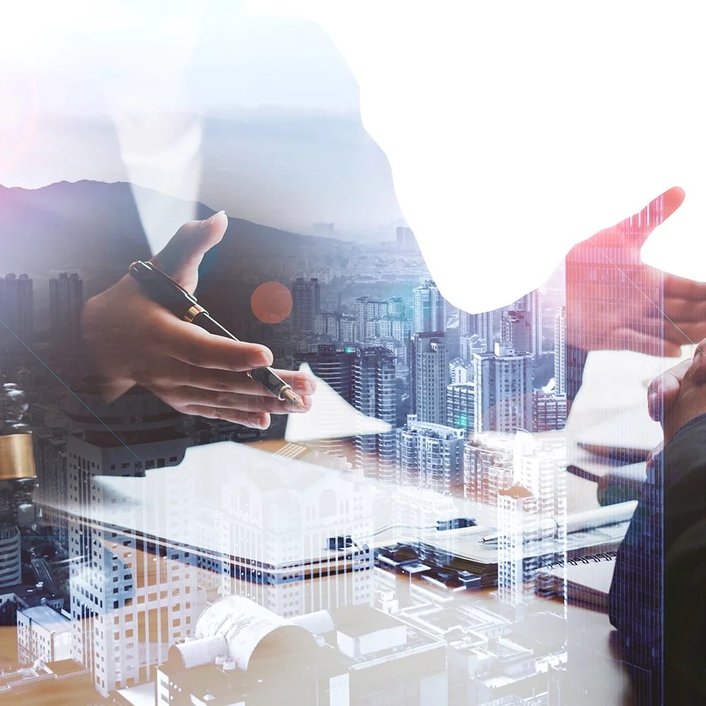 A double exposure image of two businesspeople shaking hands in an office, with a cityscape of tall buildings and mountains in the background.
