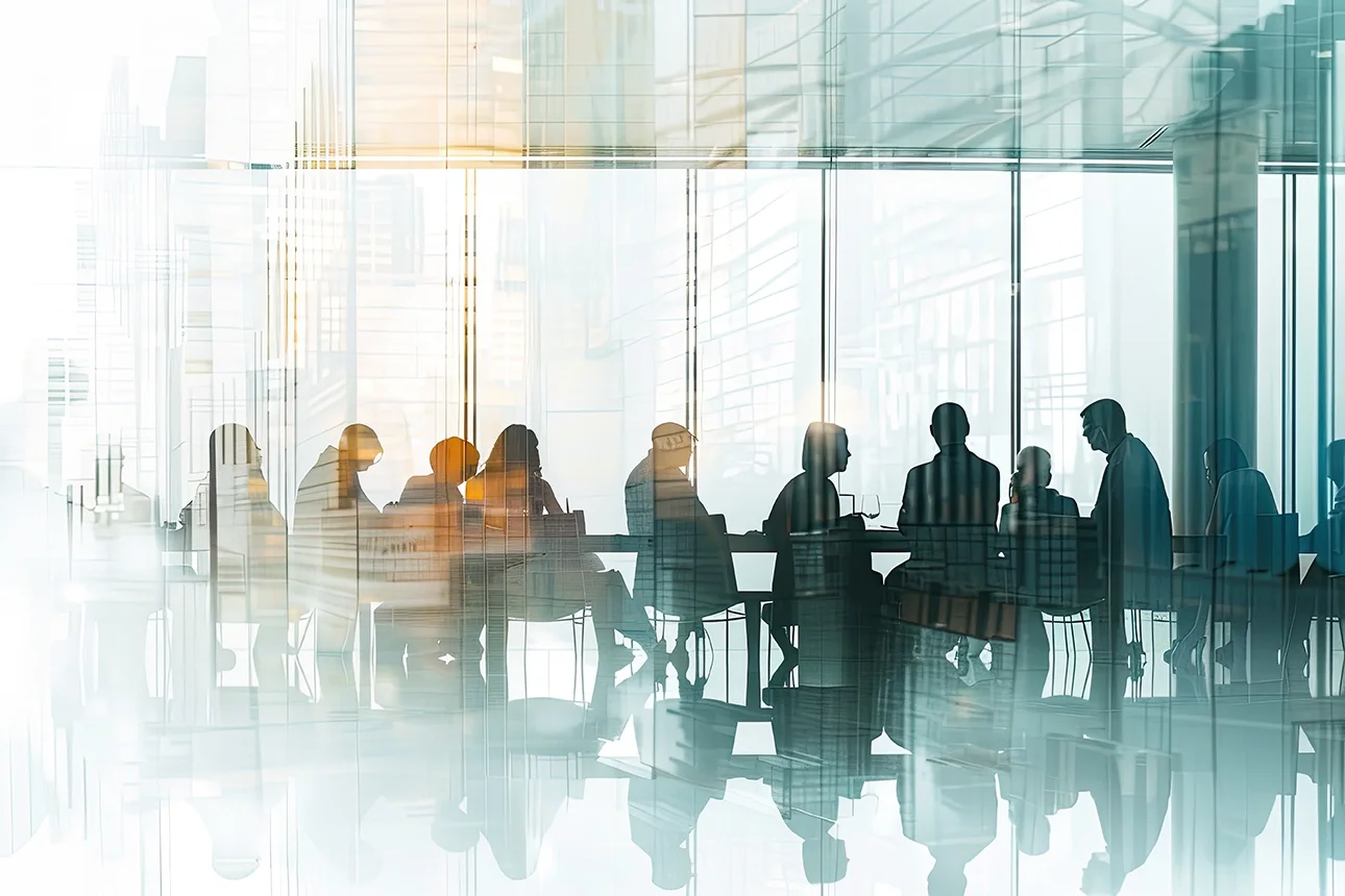 Silhouettes of business people sitting at a conference table in a modern office with floor-to-ceiling windows.