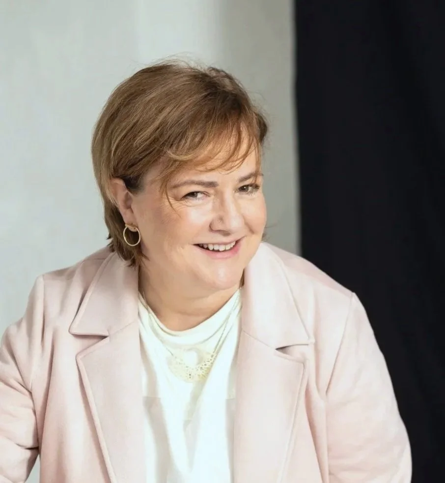 A woman with short, light brown hair wearing a light-colored blazer and smiling.
