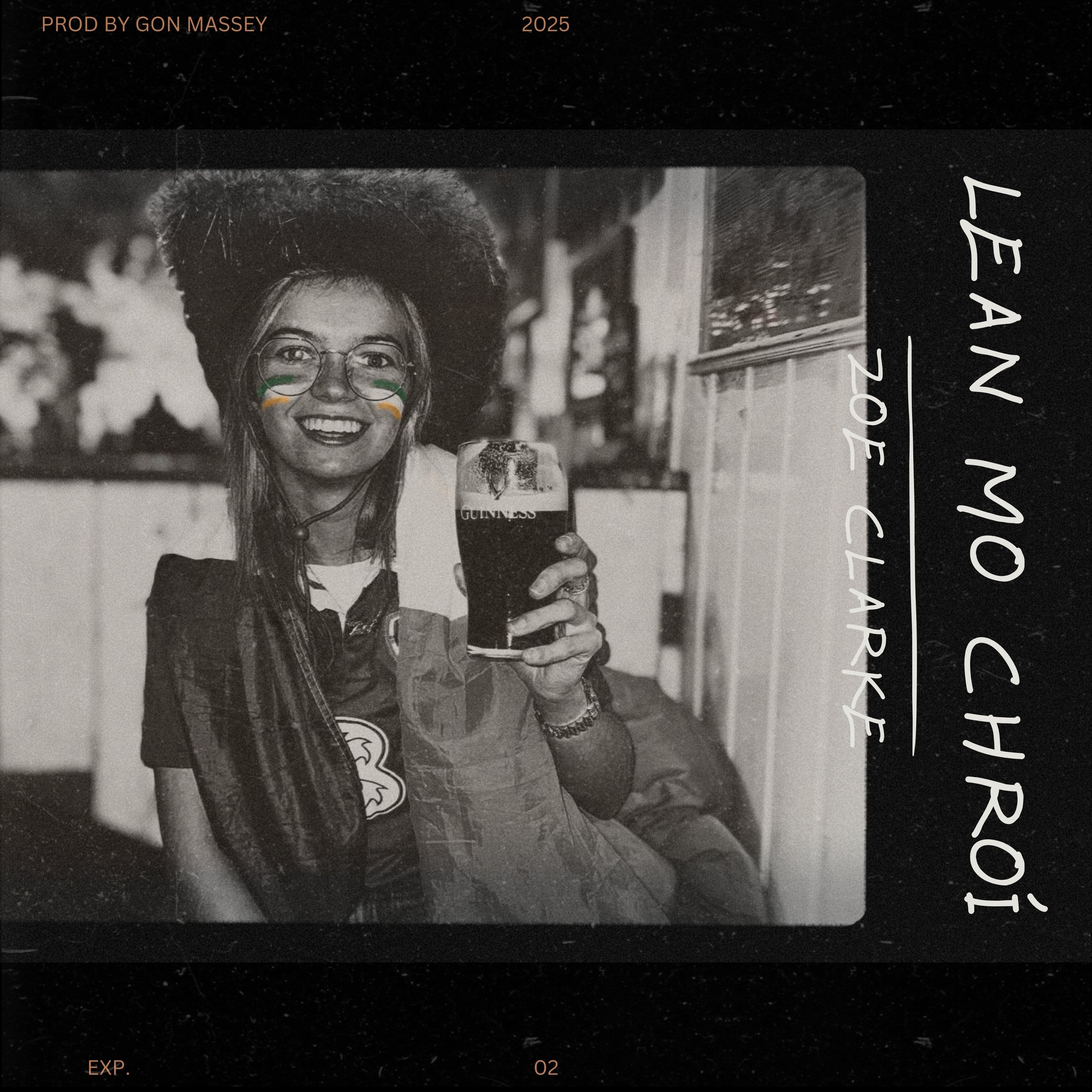Black and white photograph of a woman with glasses, painted with Irish flag colors on her cheeks, smiling and holding a Guinness beer glass, outdoors with blurred background of people and a building.