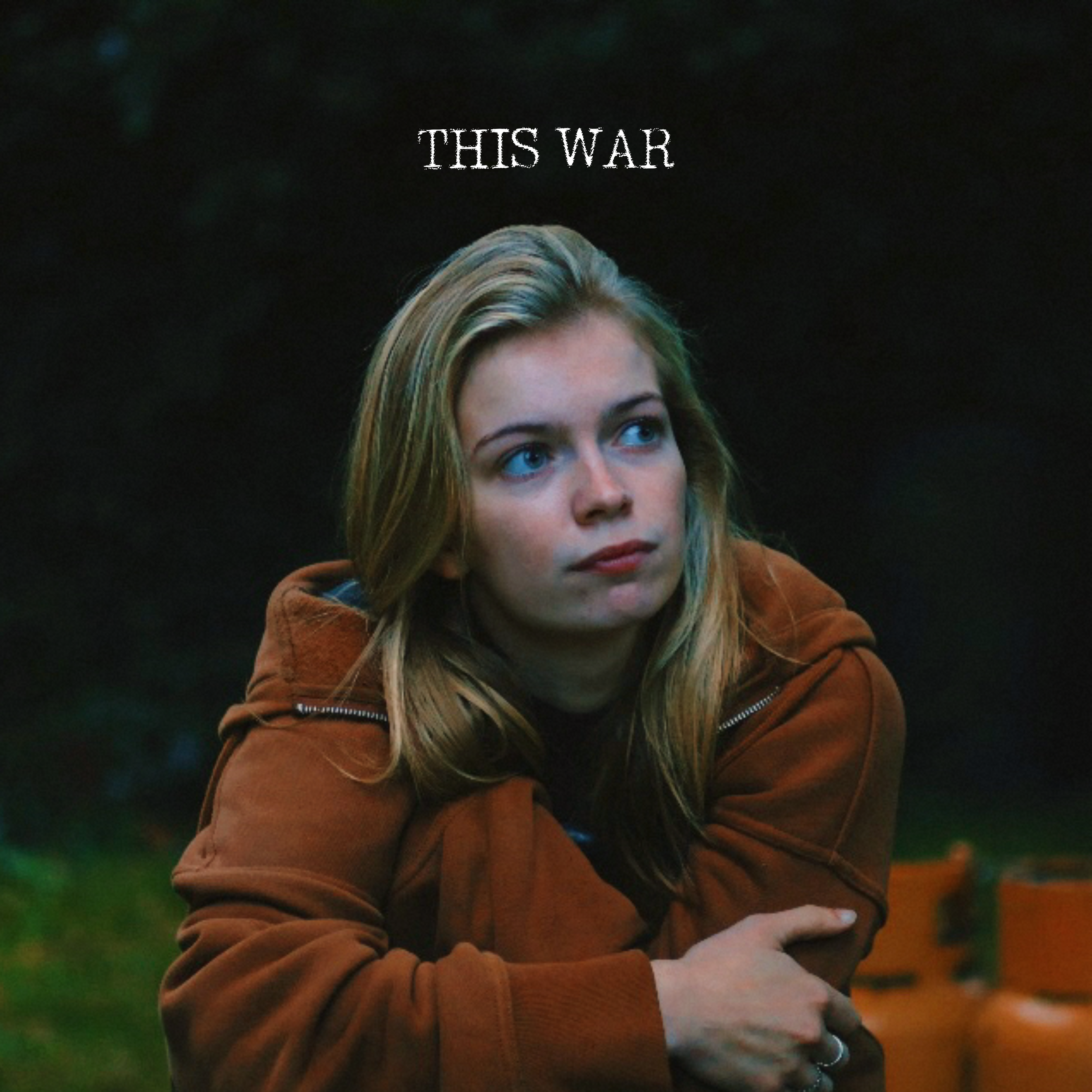 Close-up of a woman with long blond hair, wearing a brown jacket, looking to the side with a thoughtful expression, outdoors with a blurred colorful background.
