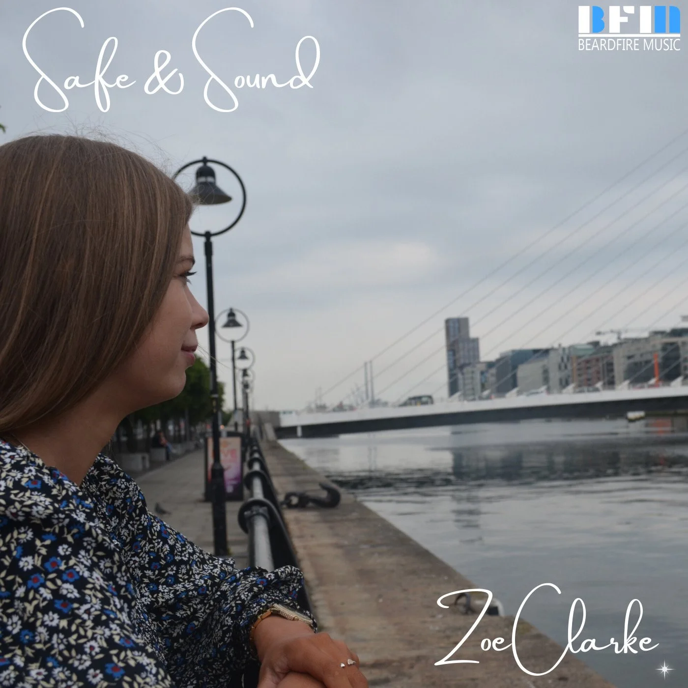 A woman with light brown hair sitting by a riverwalk, looking at the water, with city buildings and lamp posts in the background. The sky is cloudy. The text on the image reads 'Safe & Sound' and 'Zoë Clarke'.