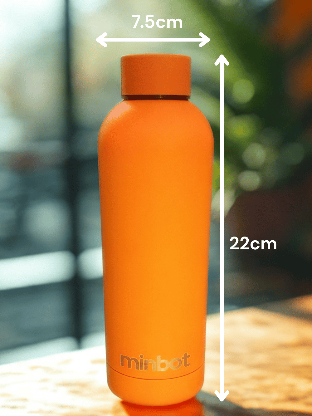 Orange water bottle with measurements indicating 7.5 cm diameter and 22 cm height, labeled 'minbot', on a wooden surface with a blurred background.