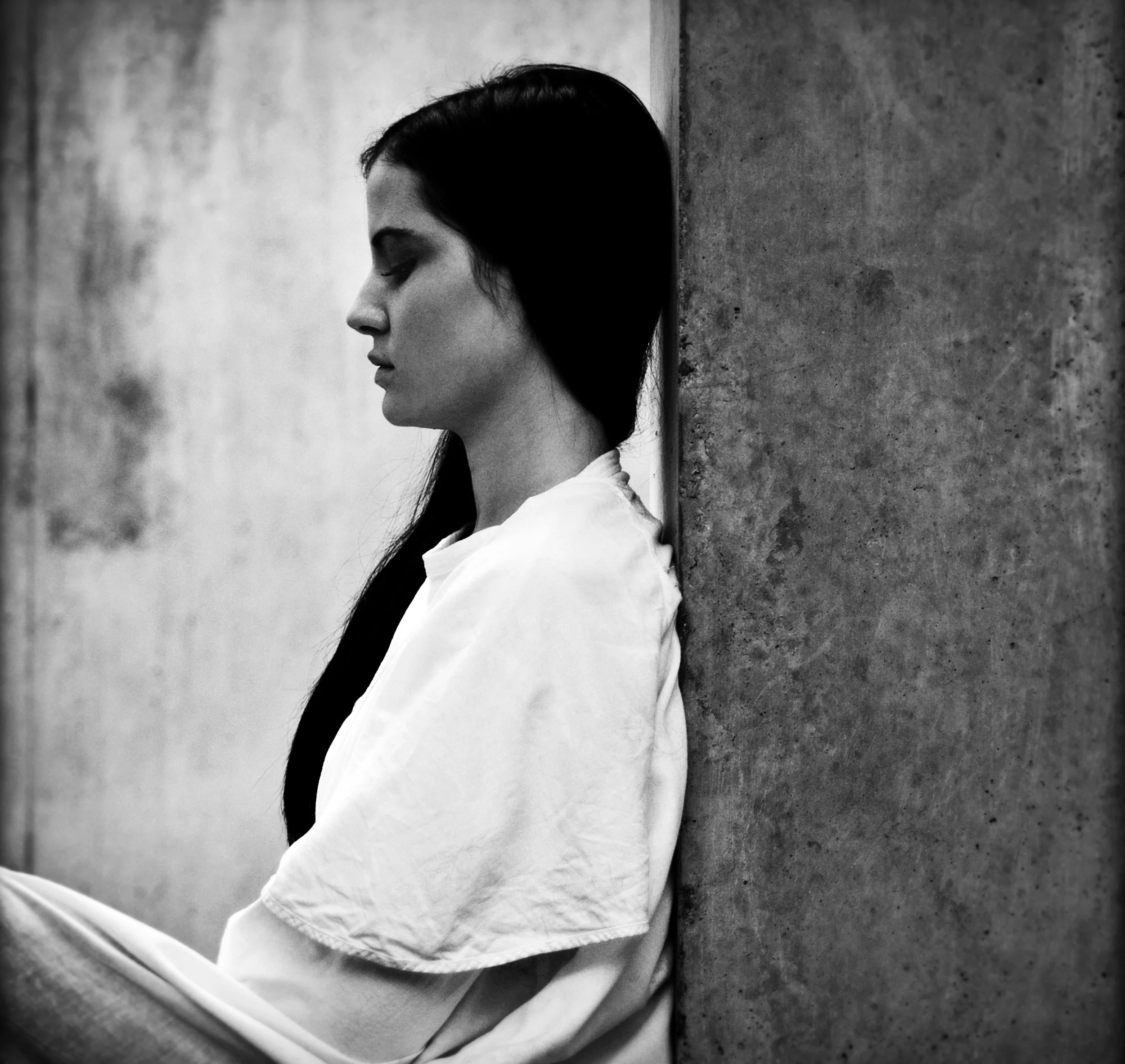 Profile portrait of a woman sitting beside a concrete wall – Postrh.