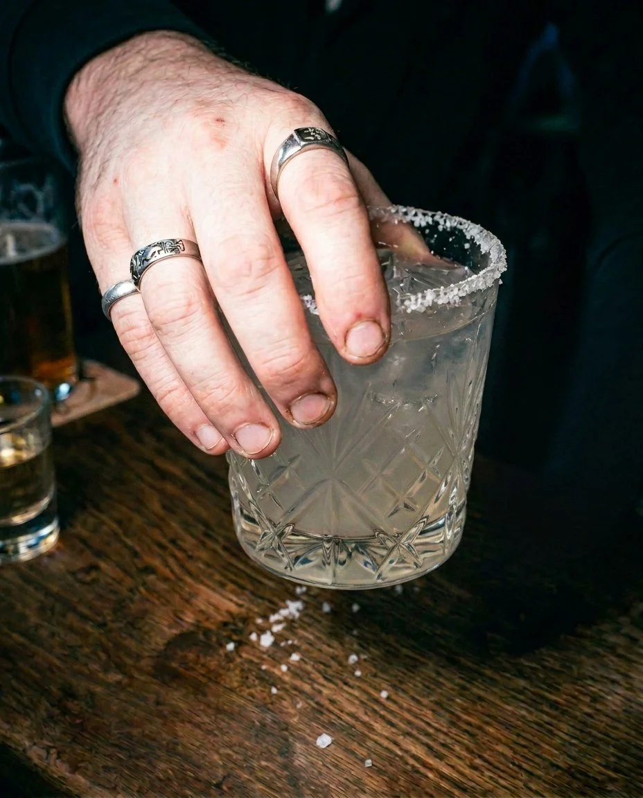 A man with tattooed fingers and a ring holding a margarita cocktail