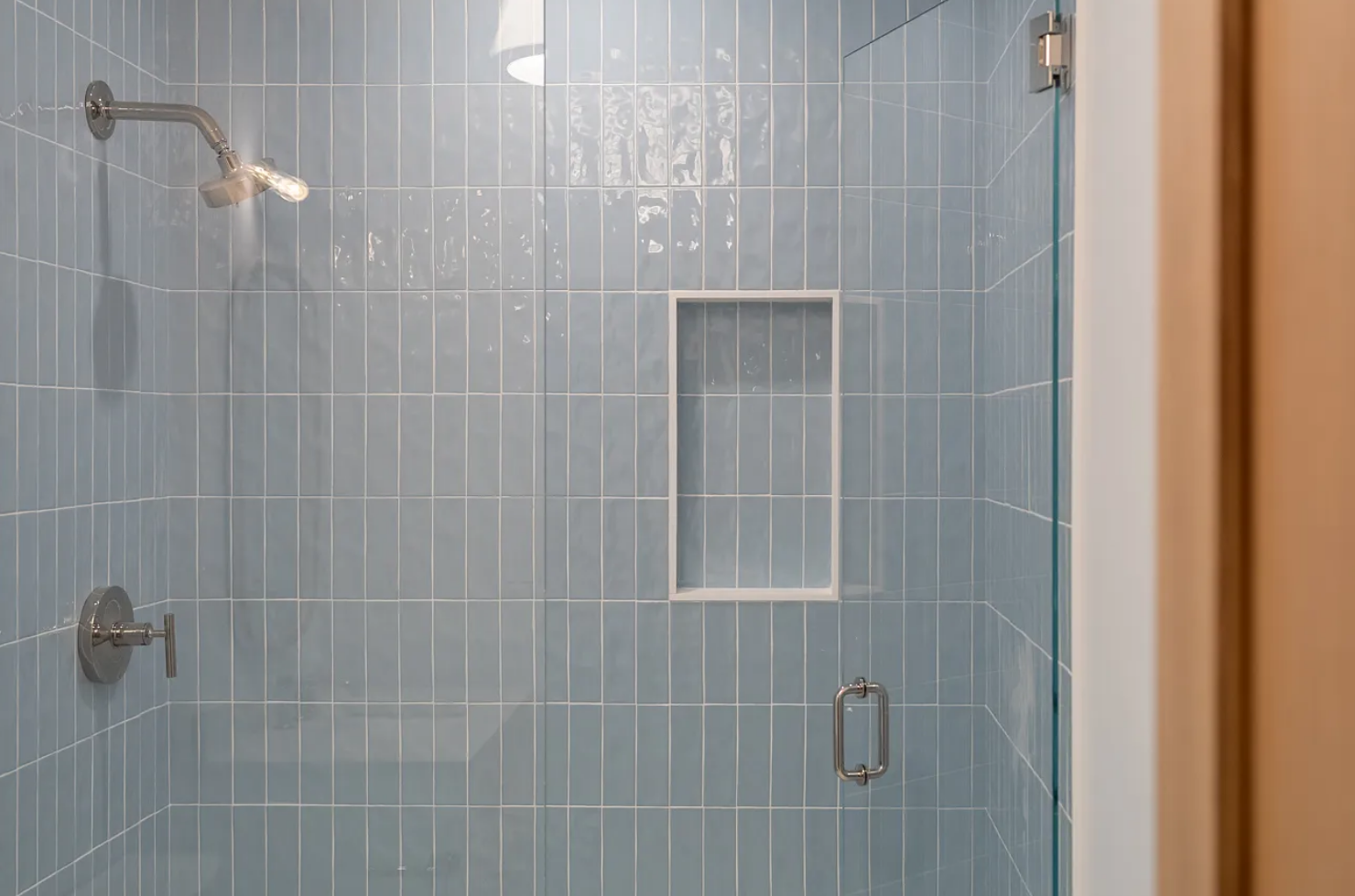 Vertical stacked blue glass tile shower with marble niche and frameless glass enclosure in a Nantucket guest bathroom.