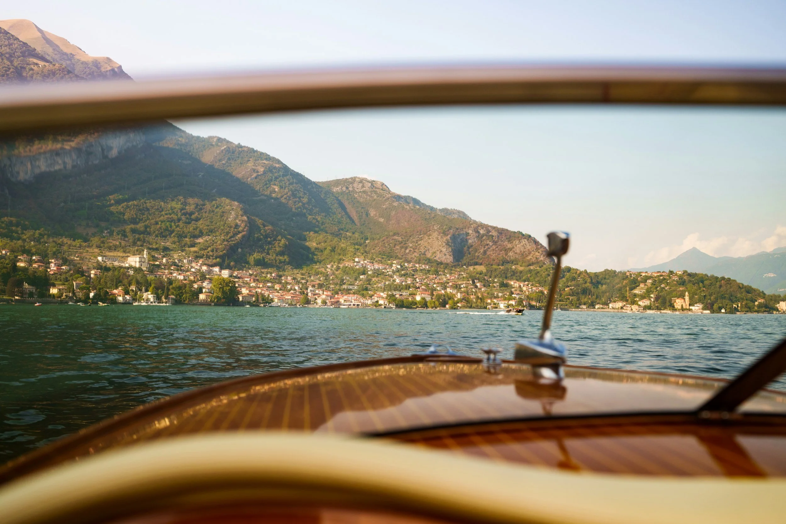 View from a boat showing a lake with mountains and a small town on the shoreline, under clear sky.