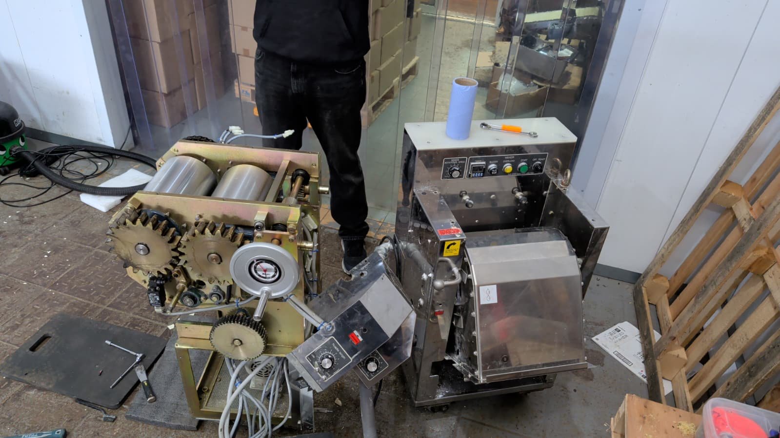 Industrial machinery and worker in a workshop, with various gears, wires, and tools around.
