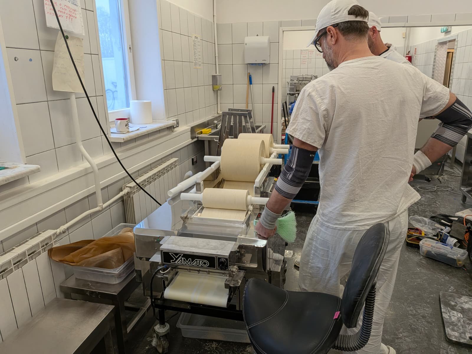 Man operating a dough or pastry rolling machine in a kitchen or bakery.