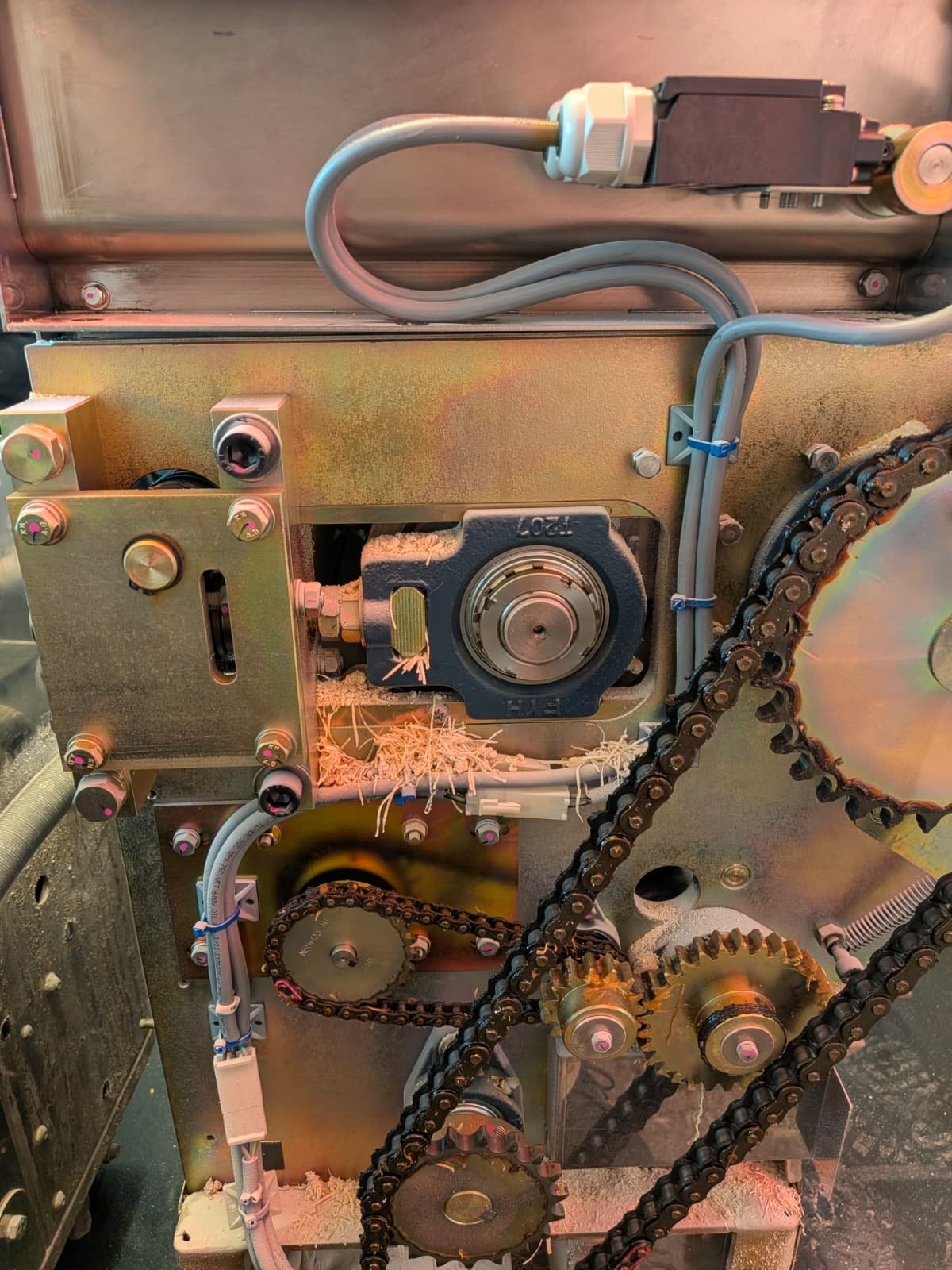 Close-up view of an internal mechanical system featuring gears, chains, electrical wiring, and metal components.