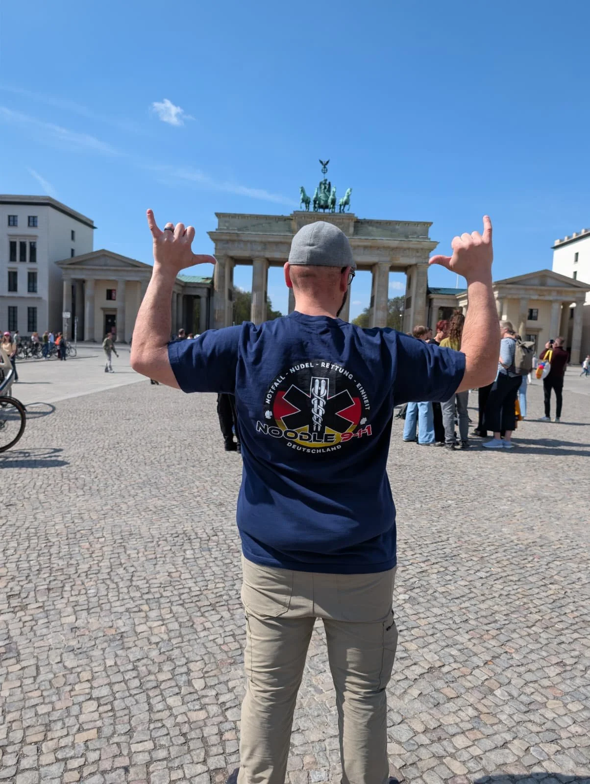 A man standing with his back facing camera, making a gesture with both hands in front of the Brandenburg Gate in Berlin, Germany.