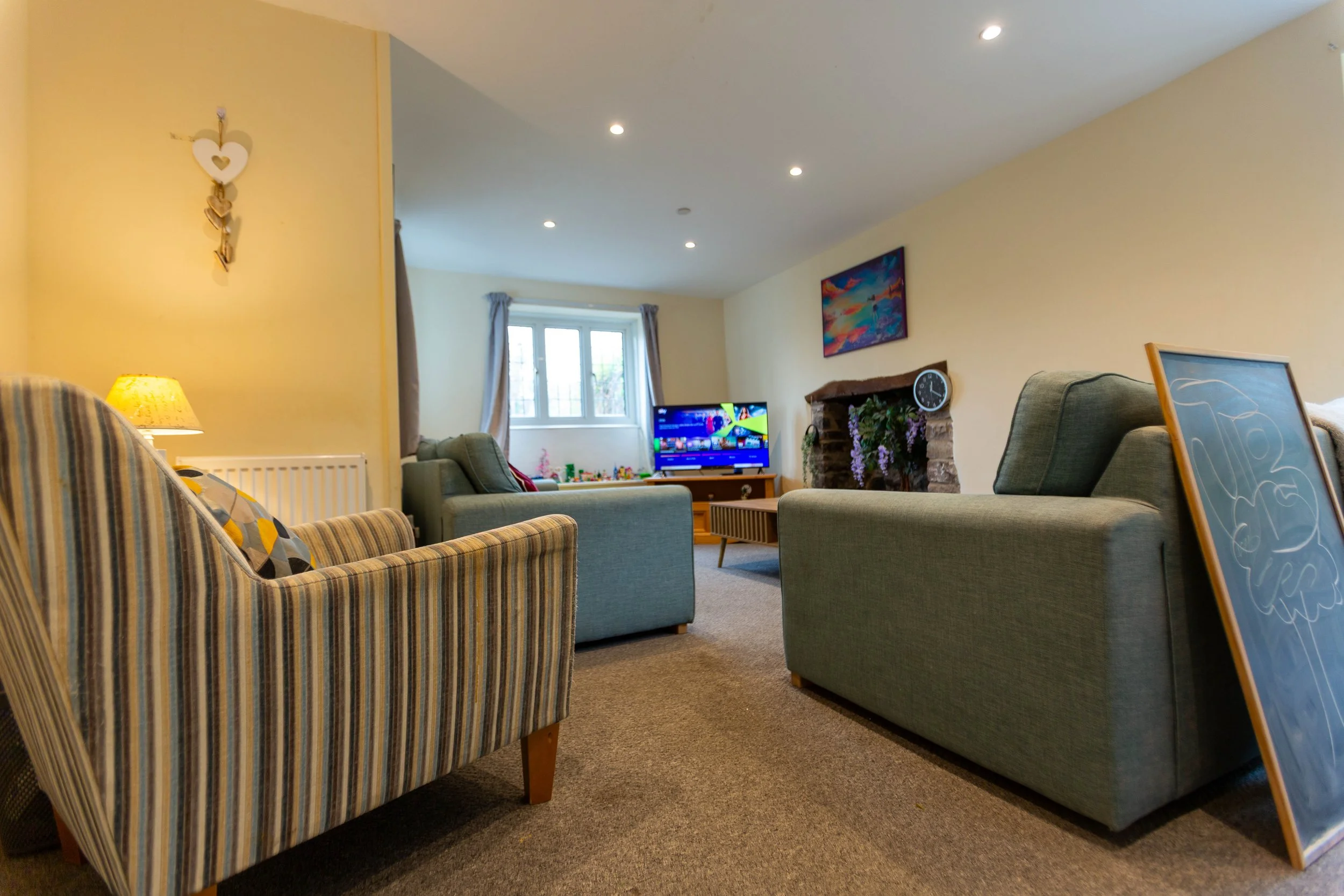 Living room with beige walls, a window with curtains, a sofa, a TV, and various decorative items.