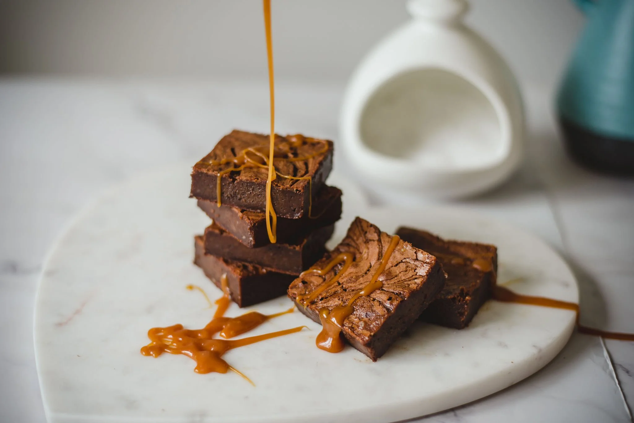 Stacked chocolate brownies drizzled with caramel on a white plate.