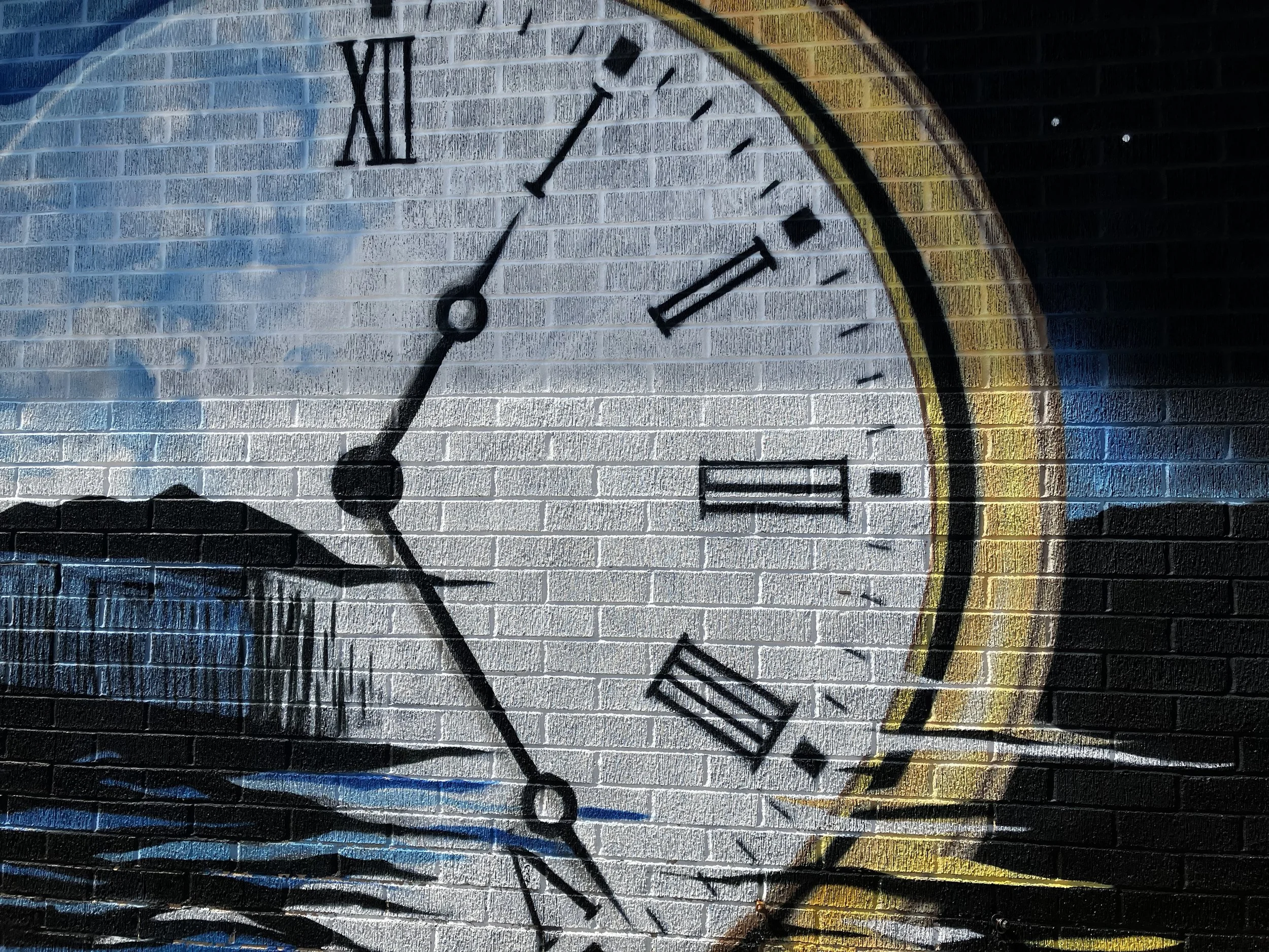 Close-up of a large clock face painted on a brick wall, showing Roman numerals and black clock hands, with some street art and graffiti in the background.