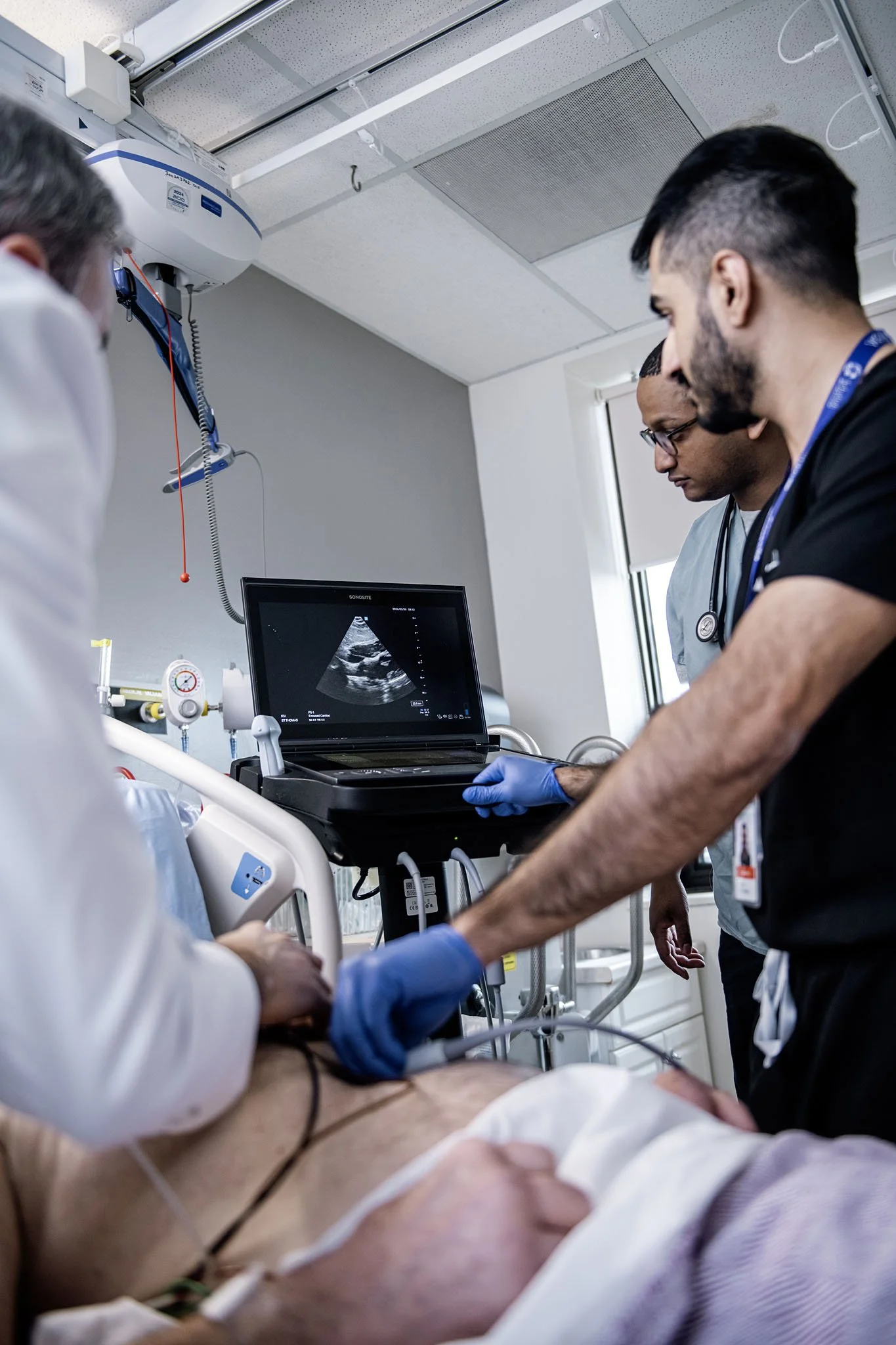 Medical professionals attending to a patient in a hospital room, with an ultrasound machine and monitors nearby.