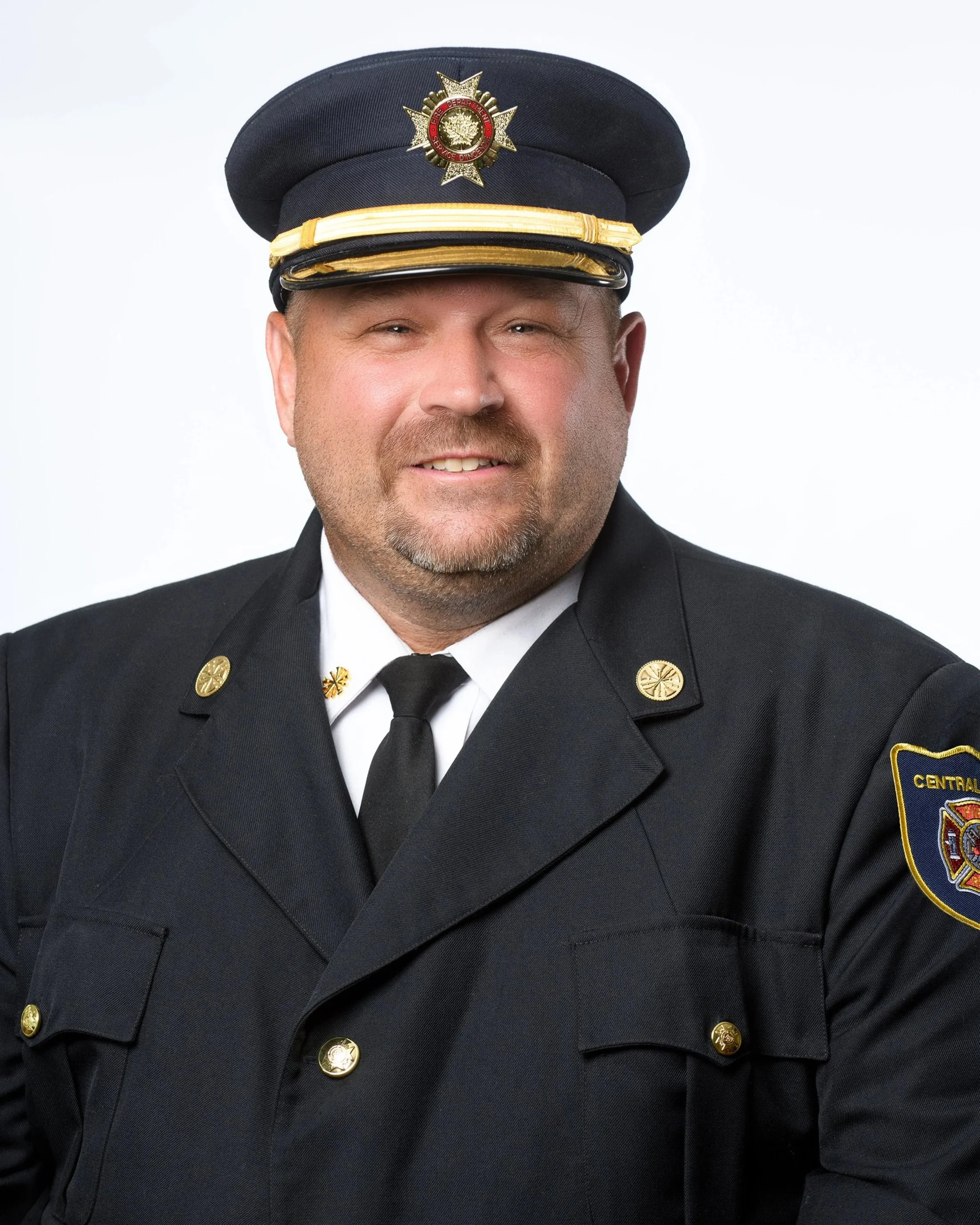 Man in a formal black police uniform, wearing a dress hat with a badge, gold accents, and a shoulder patch reading 'Central'.