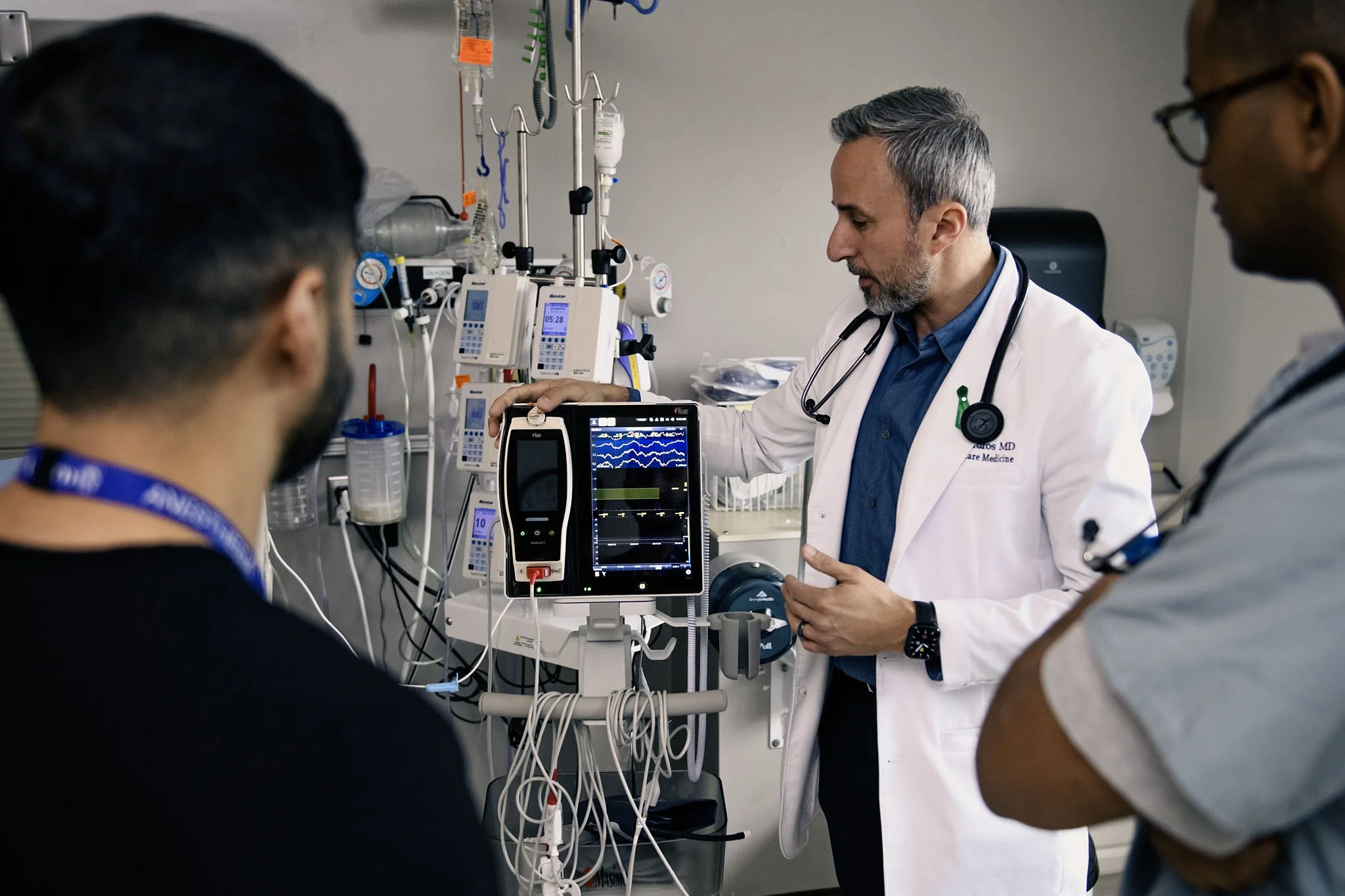 Medical professionals in a hospital room monitoring a patient on a heart rate monitor, with medical equipment and IVs in the background.