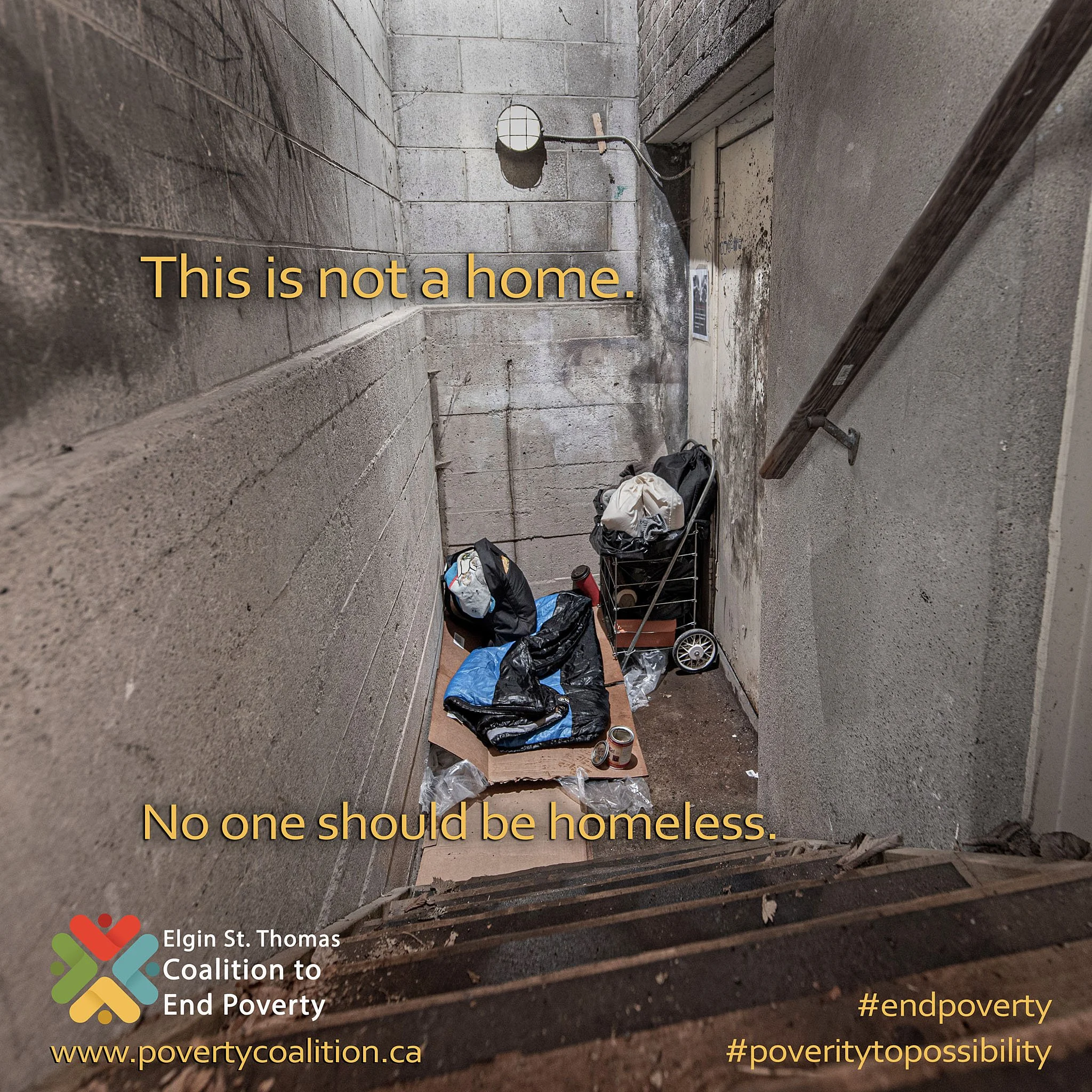 An alley with gravel ground and cinder block walls, containing scattered items including a stroller, clothing, and cans, with overlaid text that reads, 'This is not a home. No one should be homeless.'