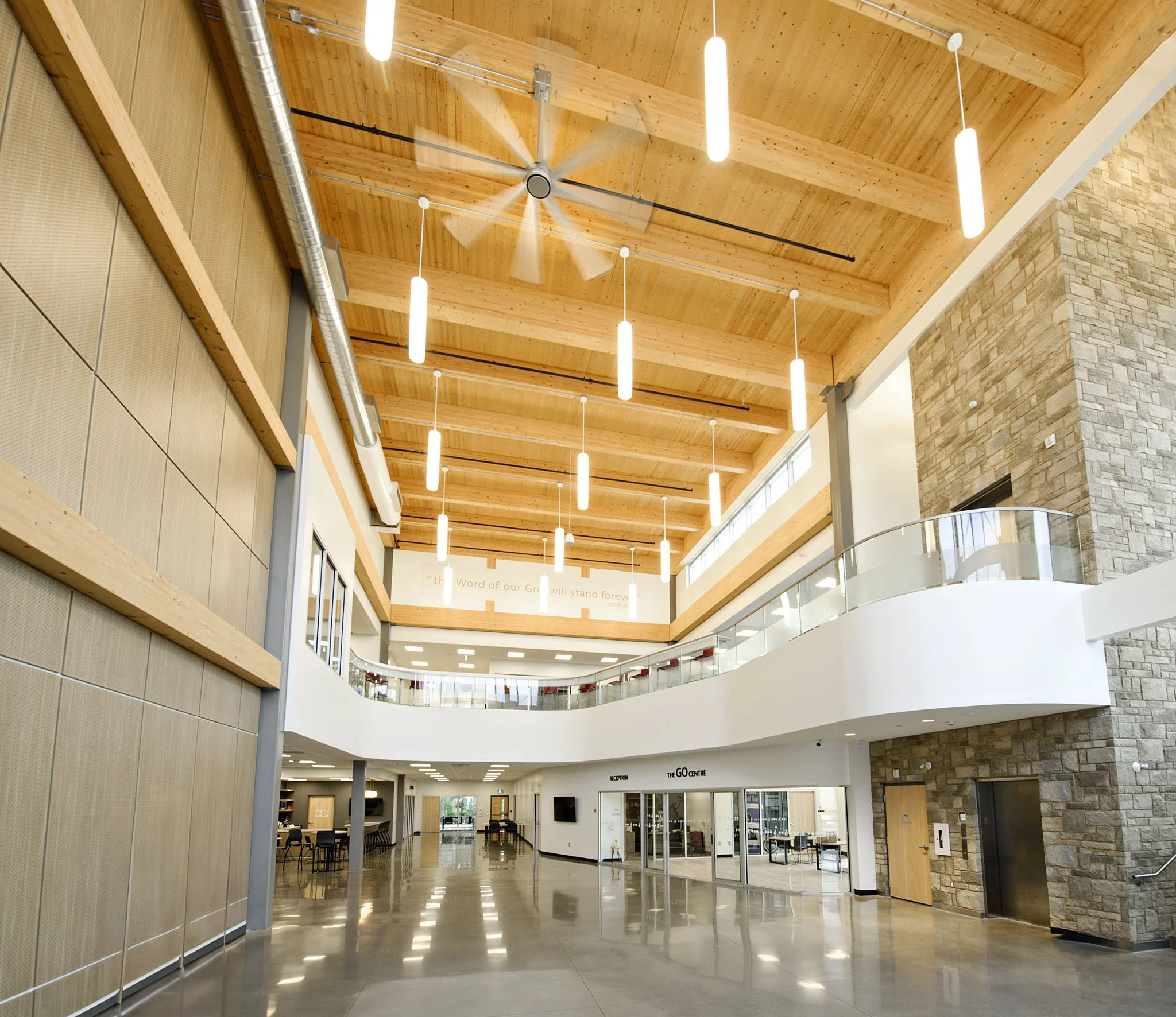 Interior of a modern building with wooden ceiling beams, hanging lights, a brick wall, and a reception area with chairs and a sign that reads 'The GO Centre'.